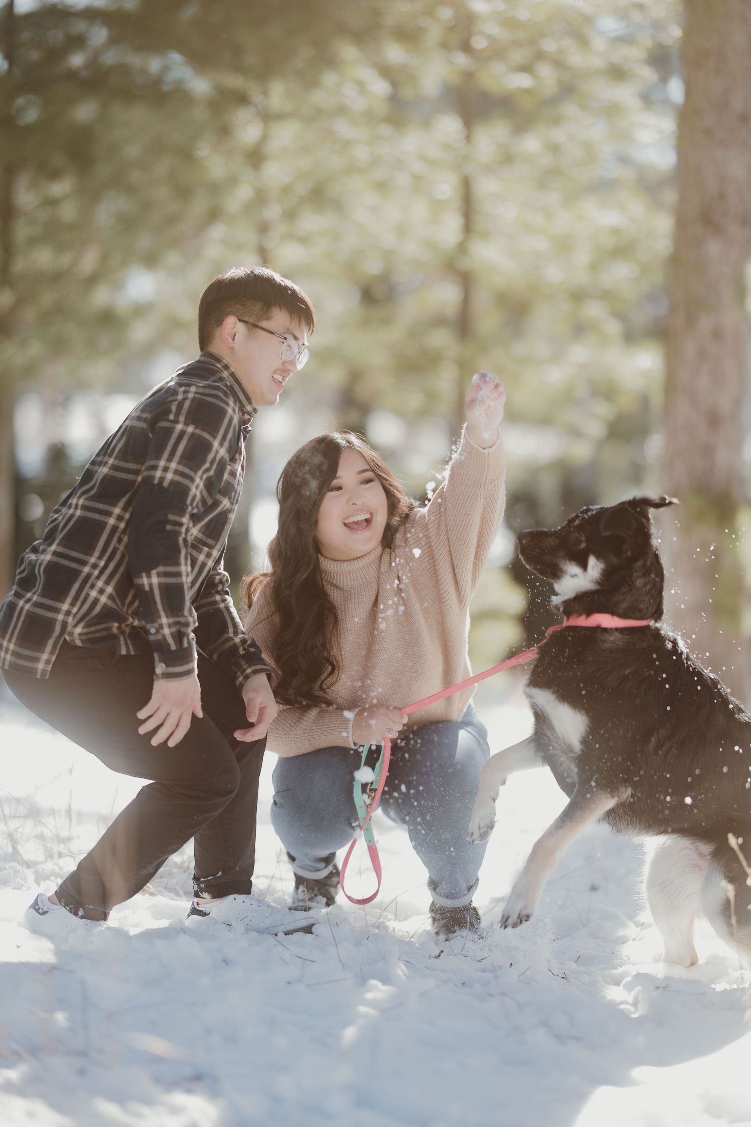 A joyful moment captured as a couple plays with their dog in the snowy forest.