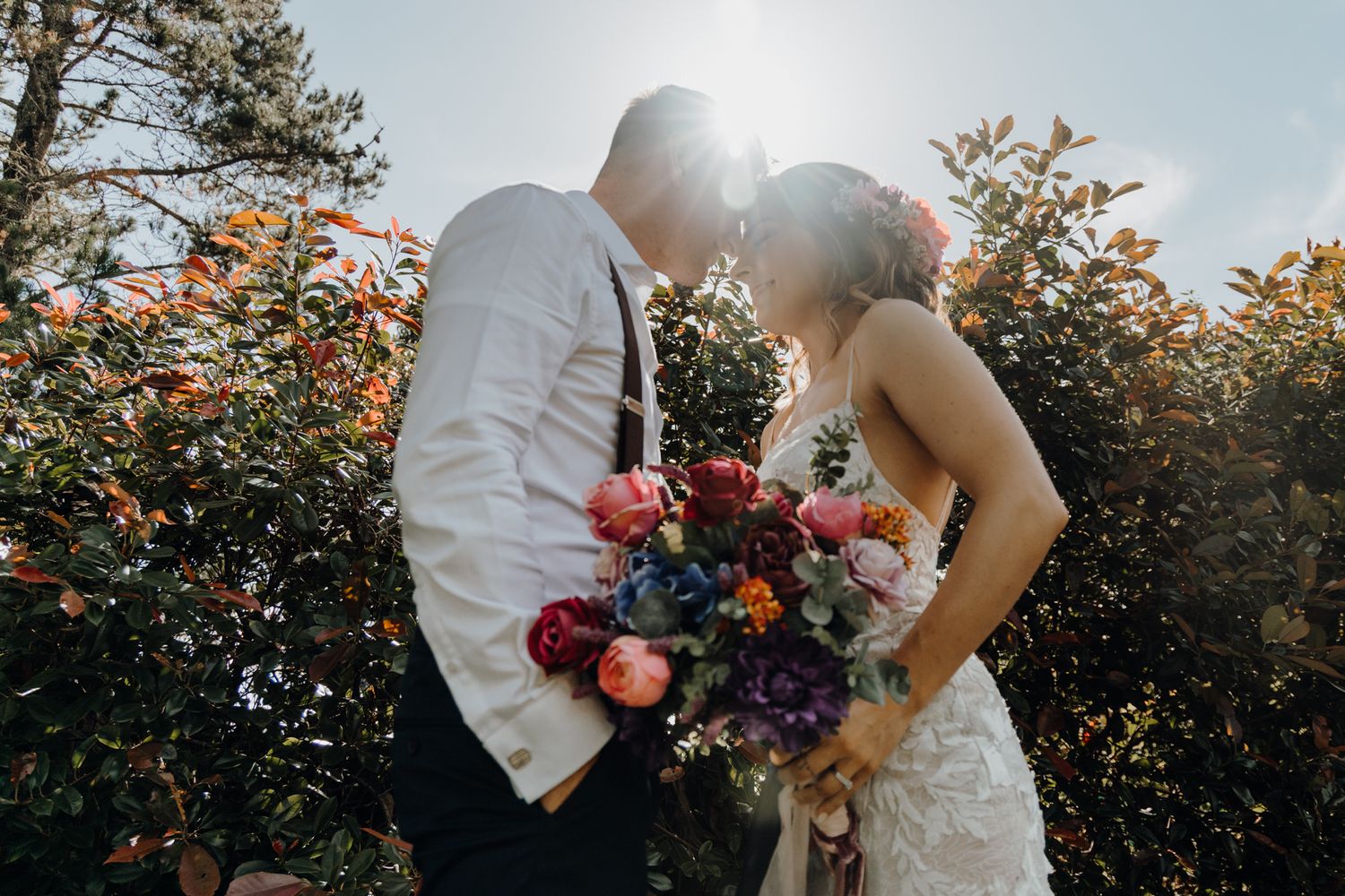 A backlit wedding portrait with a vibrant bouquet of red and purple flowers at sunset.