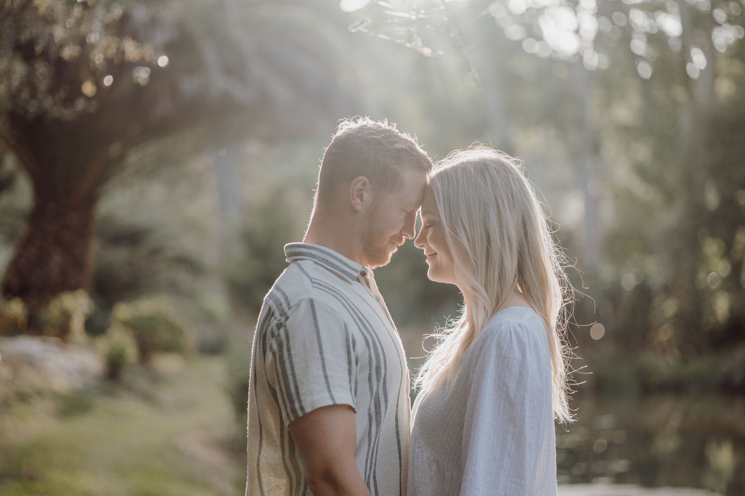A tender romantic moment between a couple backlit by golden sunlight in a garden setting.