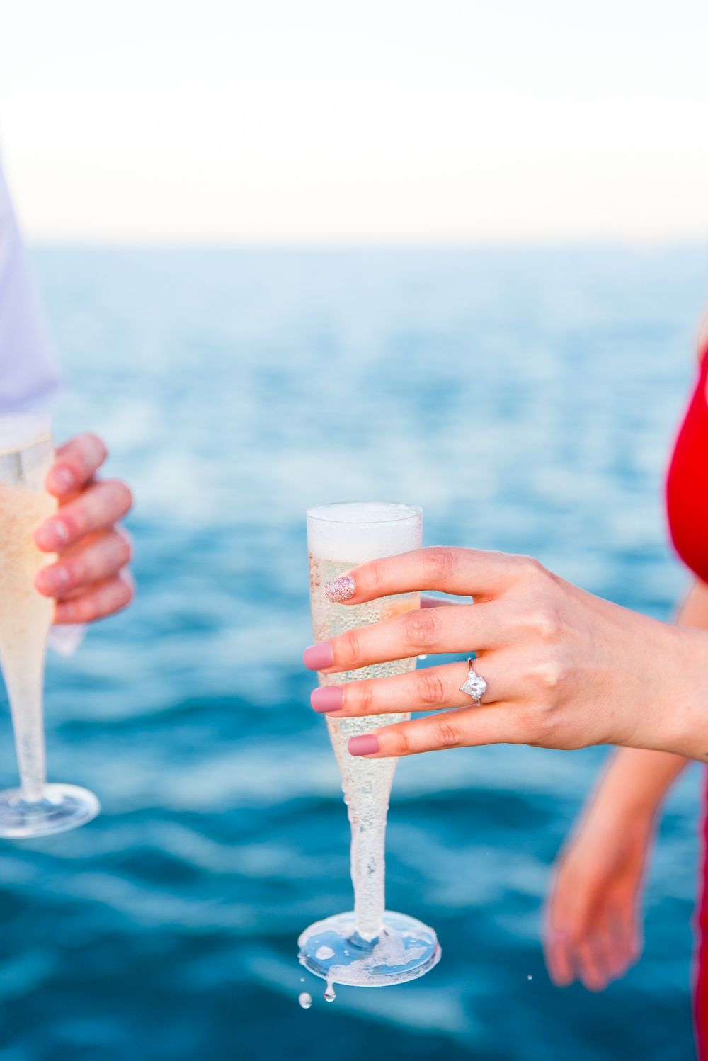 woman with engagement ring holding glass of champagne in front of Lake Michigan
