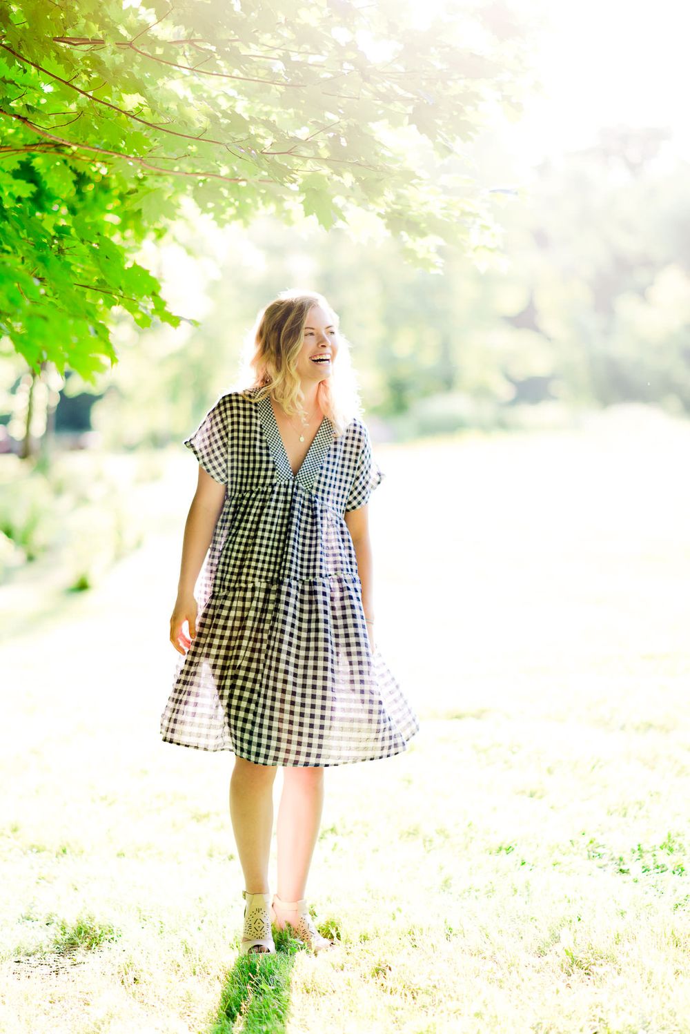 young woman in blue and white checkered dress laughing at sunset for senior pictures