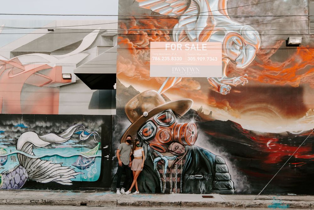 couple posing in front of a masked mural in downtown Miami