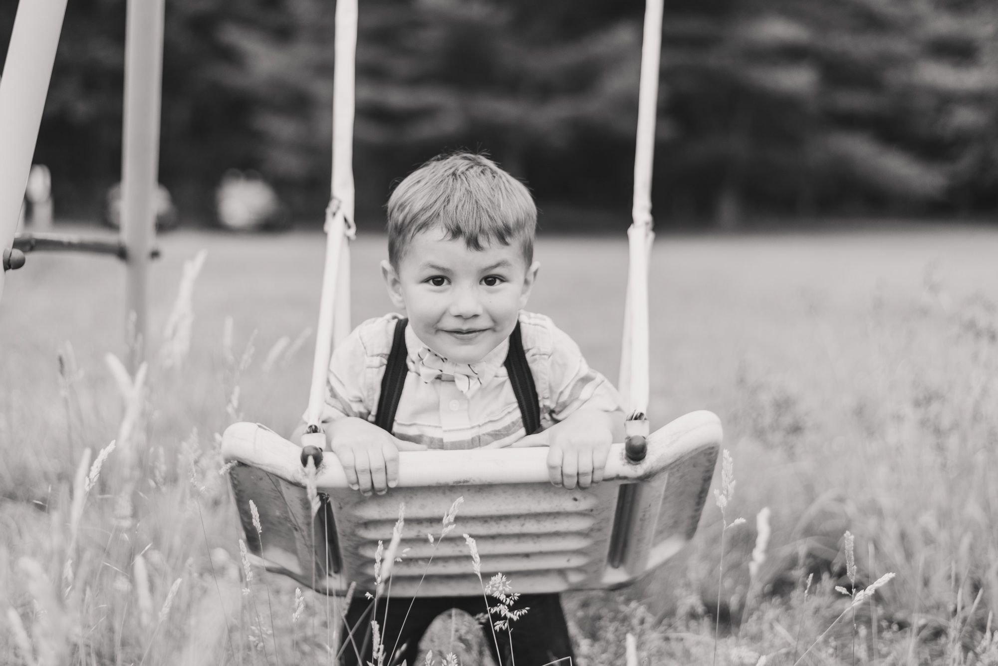 Little boy in suspenders swinging on swing set in black and white in Clarion Pennsylvania
