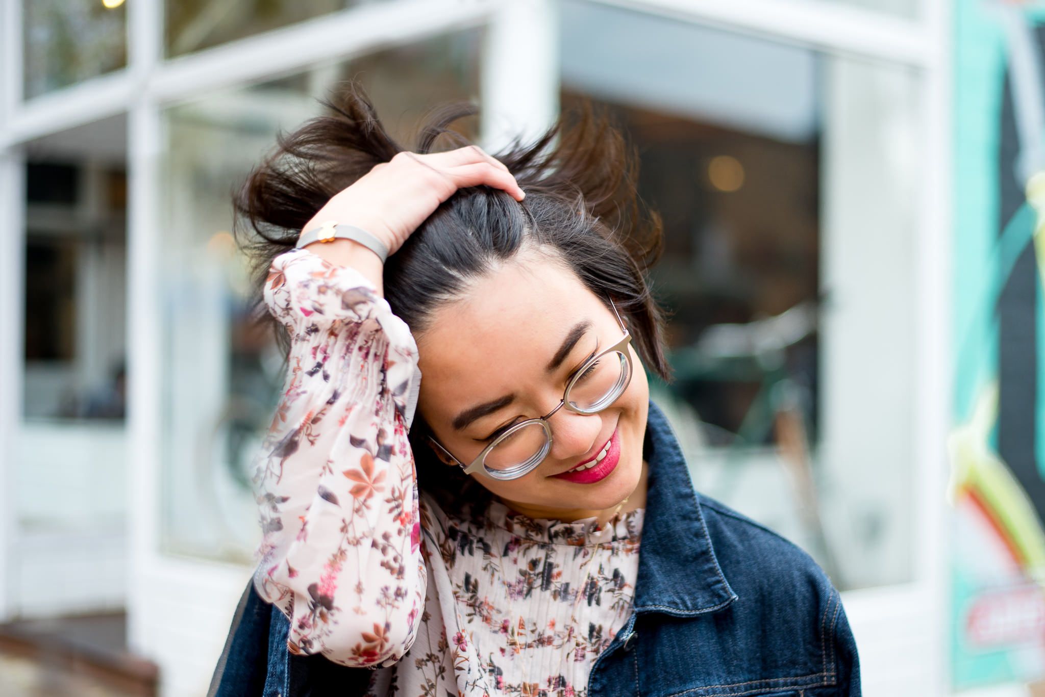 young woman in floral shirt and glasses flipping her hair
