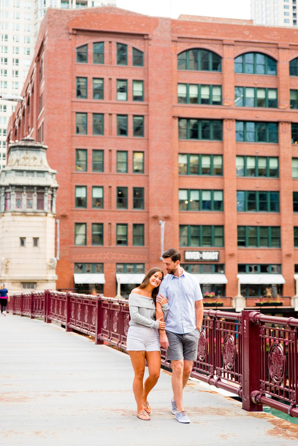 woman in gray sweater and white shorts hugging fiance's arm and walking across LaSalle Street Bridge