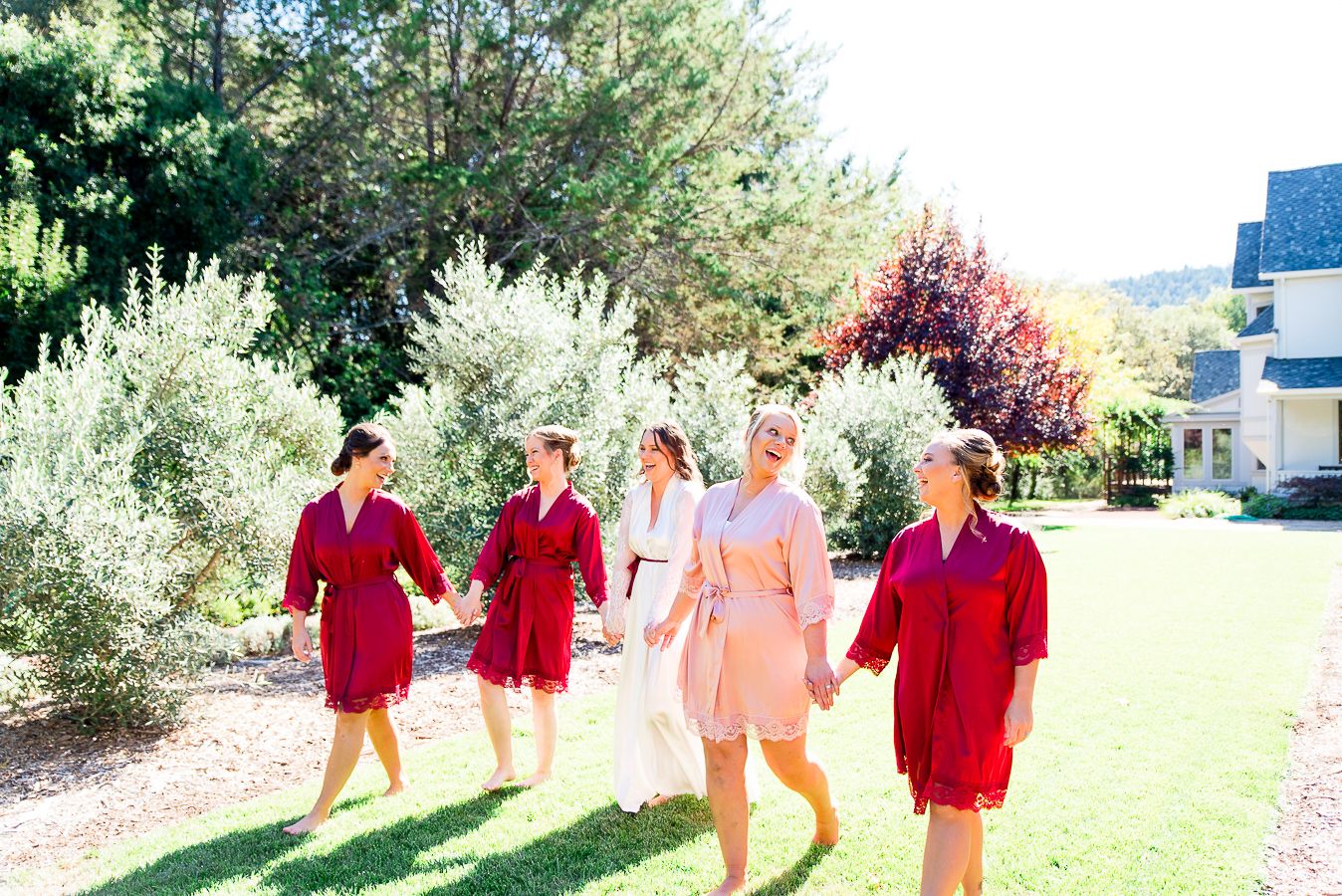 bridesmaids in red and blush robes walking in yard in California AirBNB
