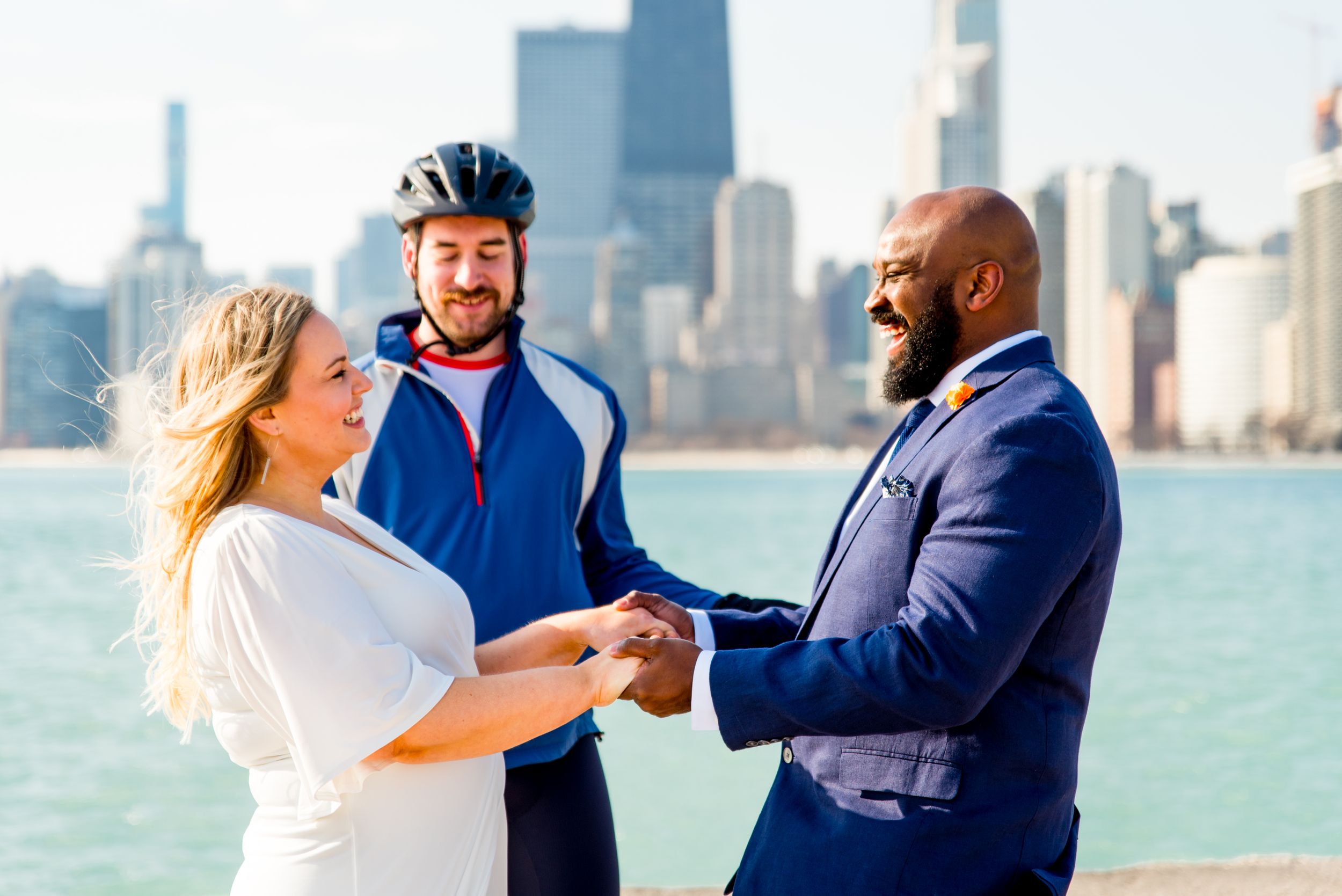 man and woman laughing holding hands as friend in biking outfit marries them at north avenue beach elopement