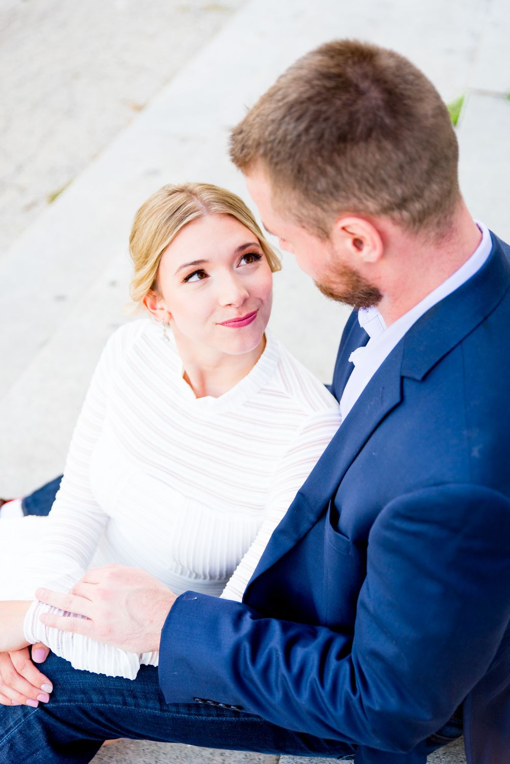 blonde woman in white smiles at fiancee in navy suit in Millennium Park Chicago
