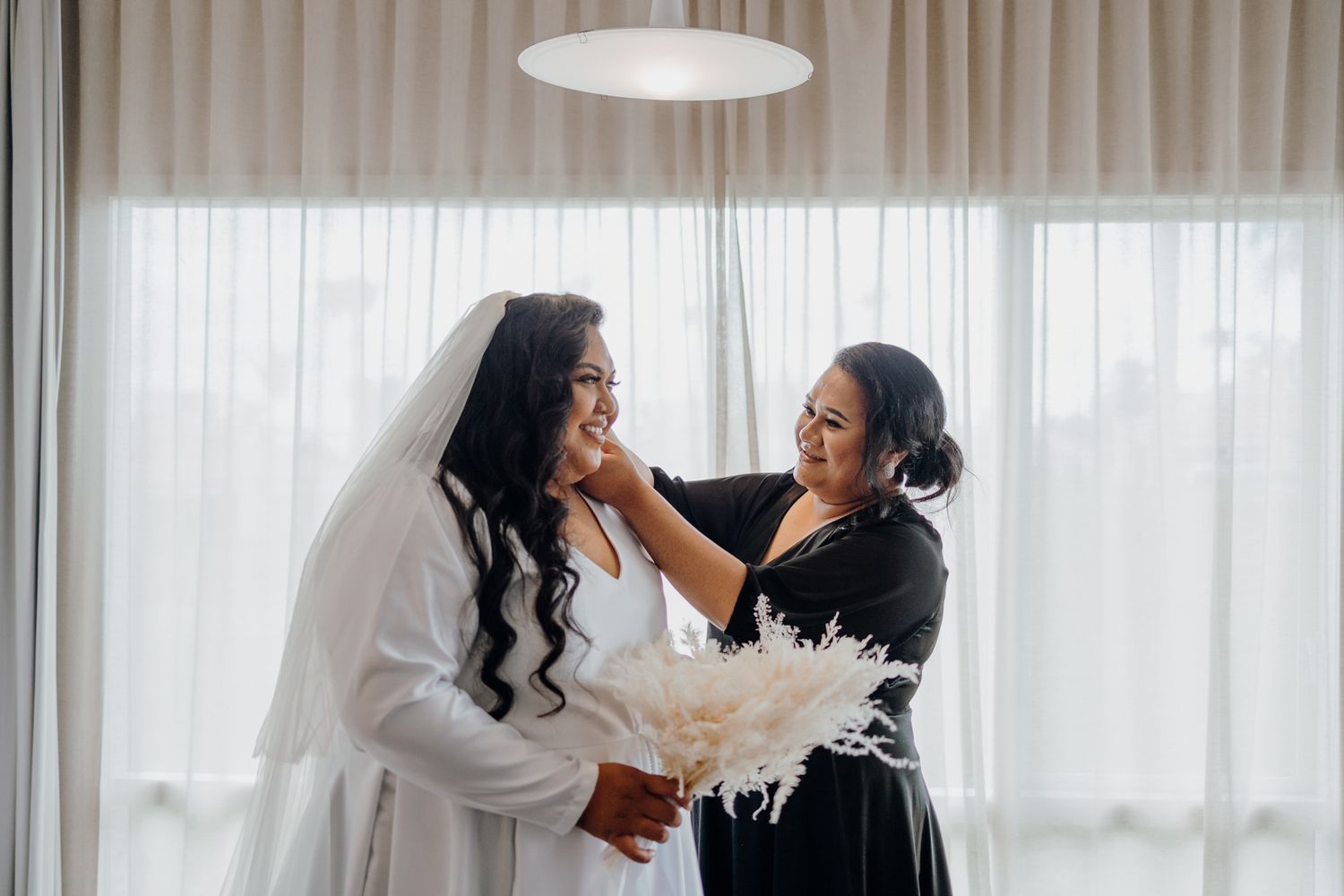 An intimate getting ready moment between two people during wedding preparations with white decor.