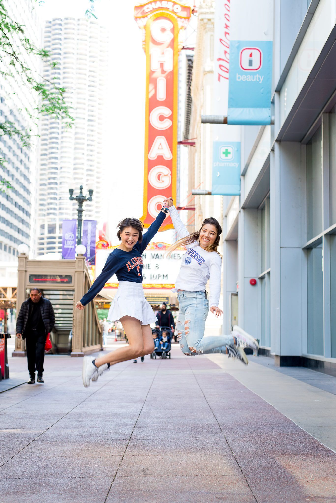 two senior girls jumping in front of the Chicago Theater sign for Chicago senior pictures