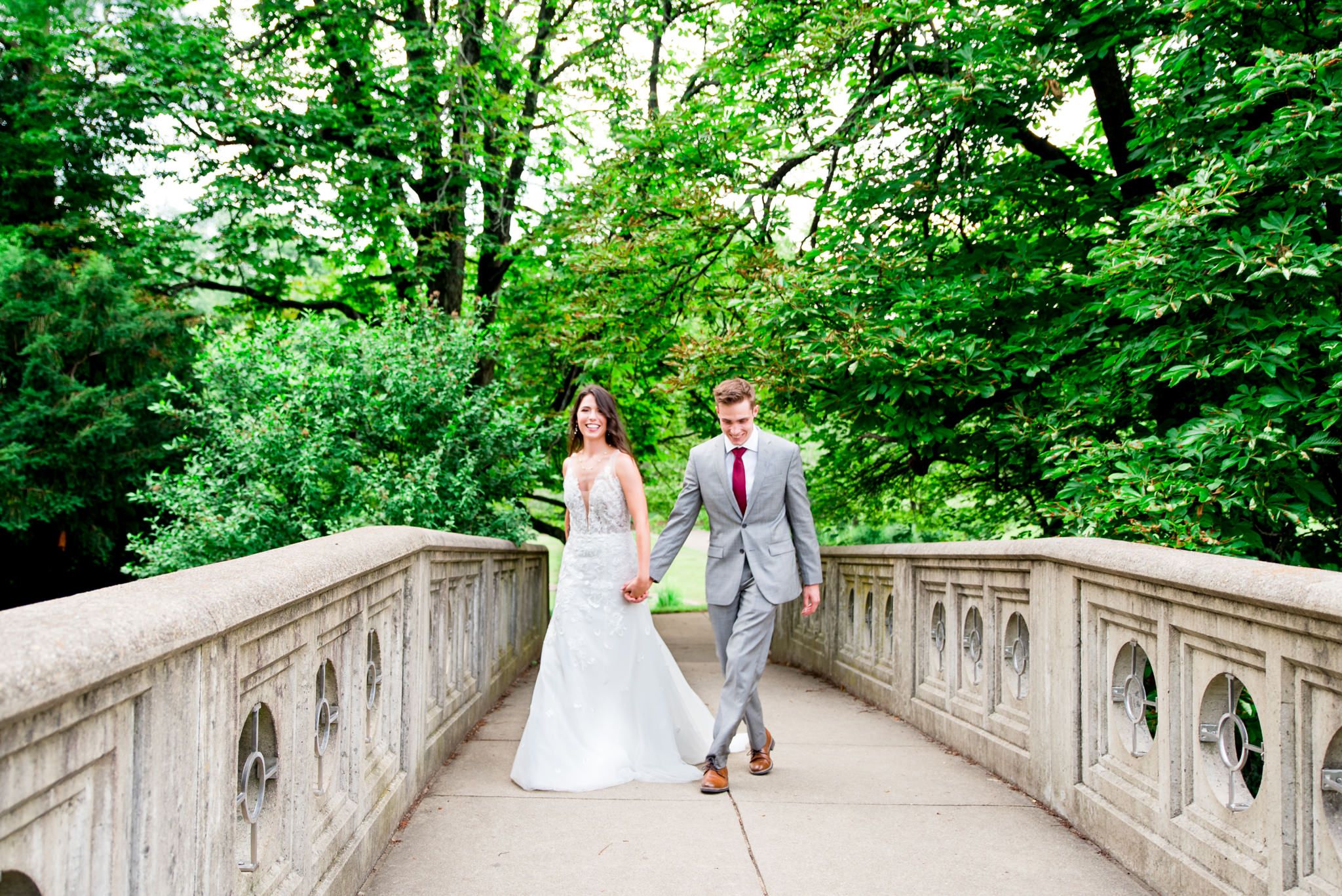 Bride and groom in gray suit walking across bridge at Eden Park in Cincinnati