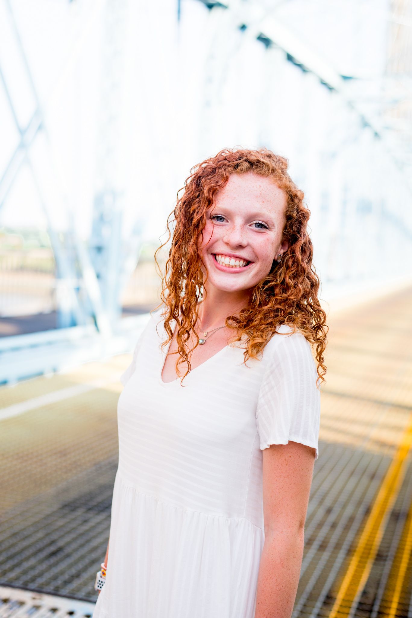 young woman with curly red hair smiling in front of blue Roebling Bridge for downtown Cincinnati senior pictures