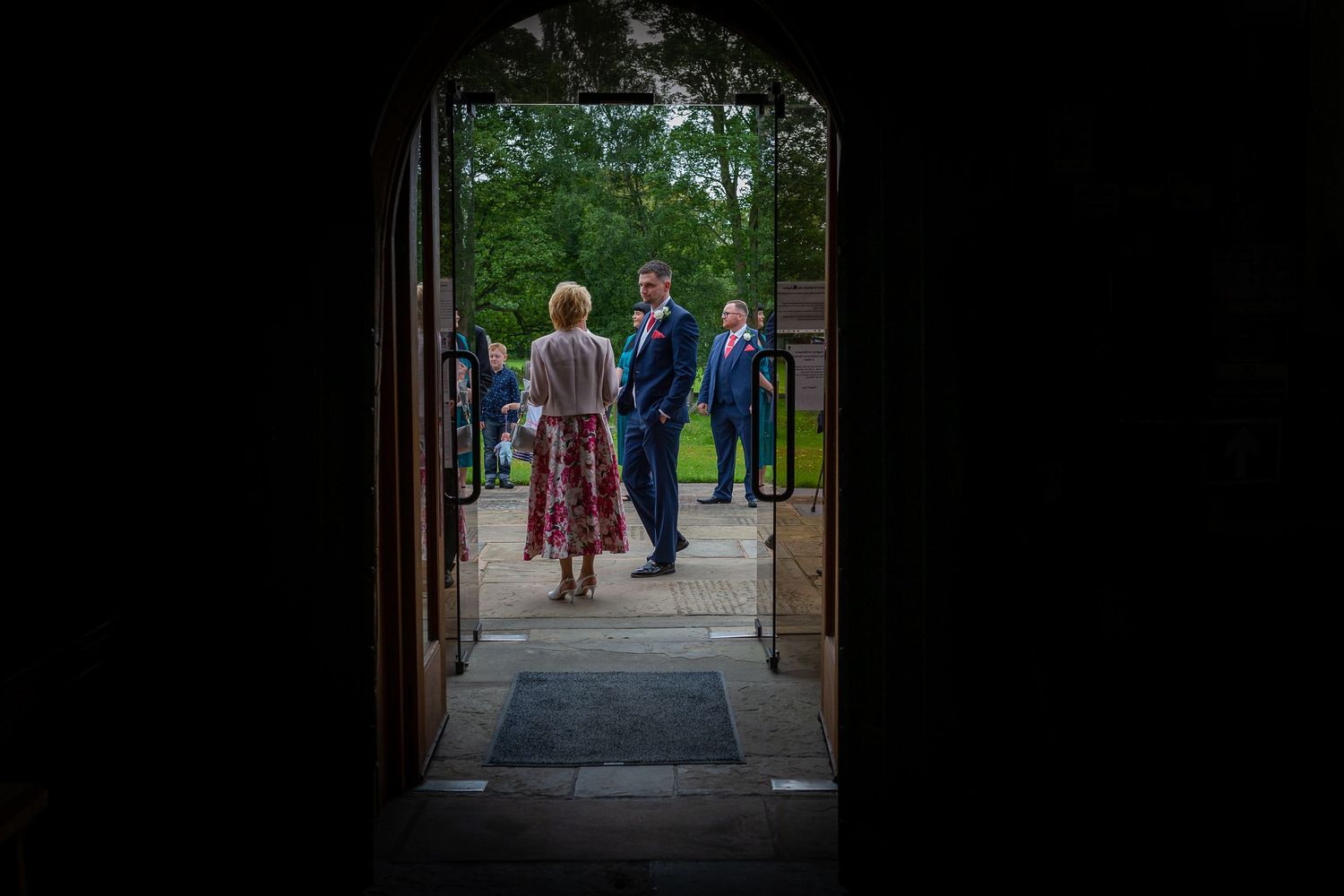Photograph of the groom and wedding guests outside the church taking from the inside