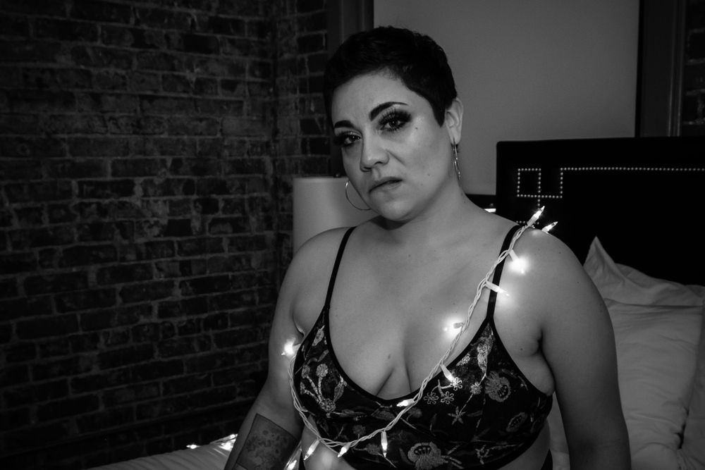 A moody boudoir portrait with string lights and exposed brick background.