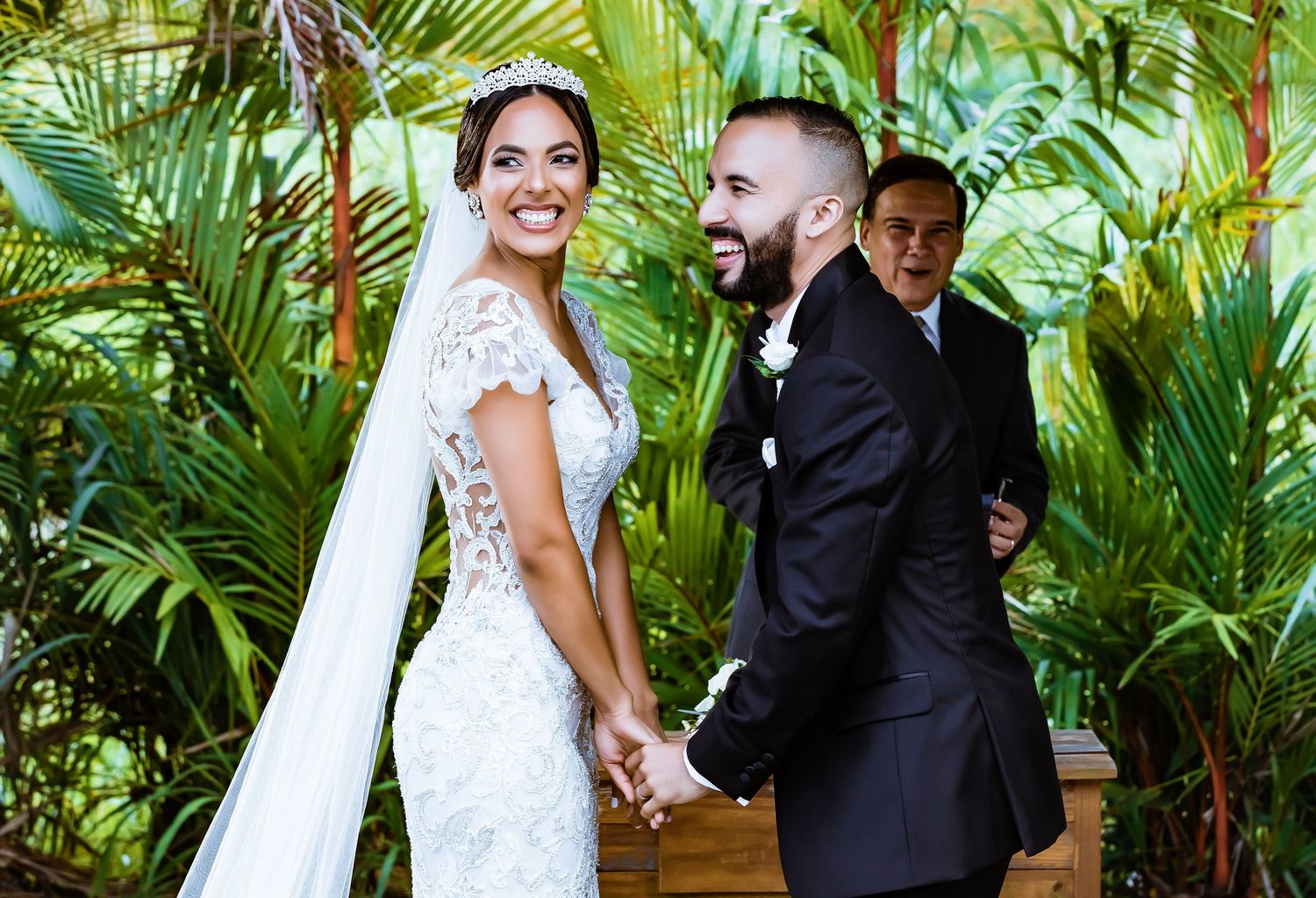 Newlywed couple shares joyful moment among tropical palm plants during wedding ceremony.