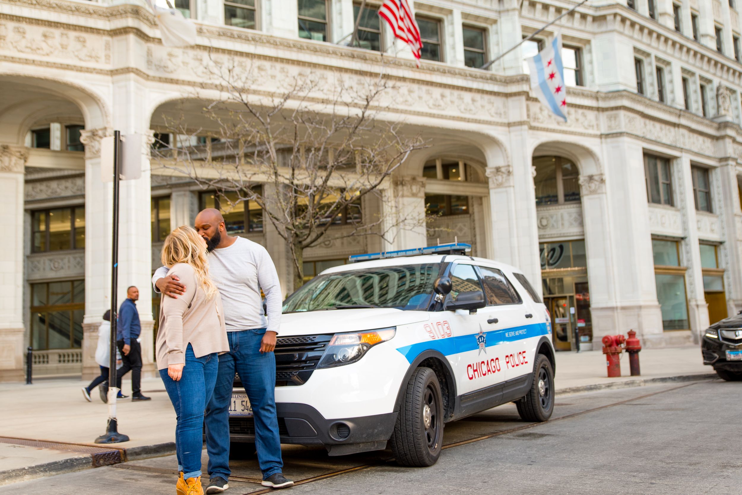 man and woman kissing in front of cop car at Wrigley Building for engagement photos in Chicago