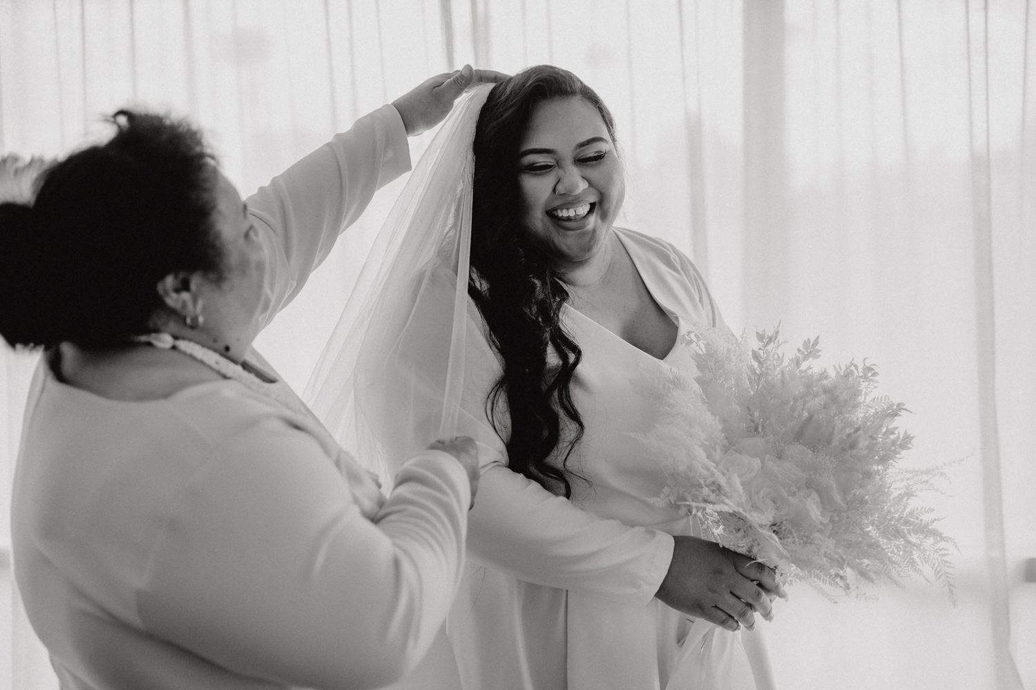 A heartwarming bridal preparation moment as the veil is adjusted while holding a white bouquet.