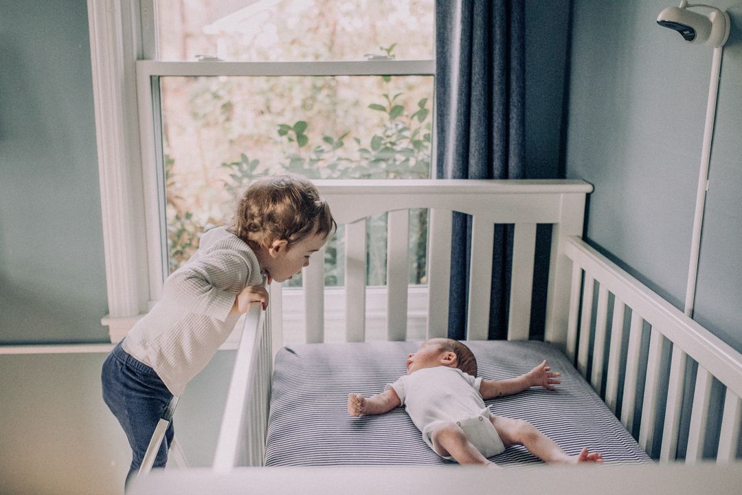 sister peeking on newborn baby brother