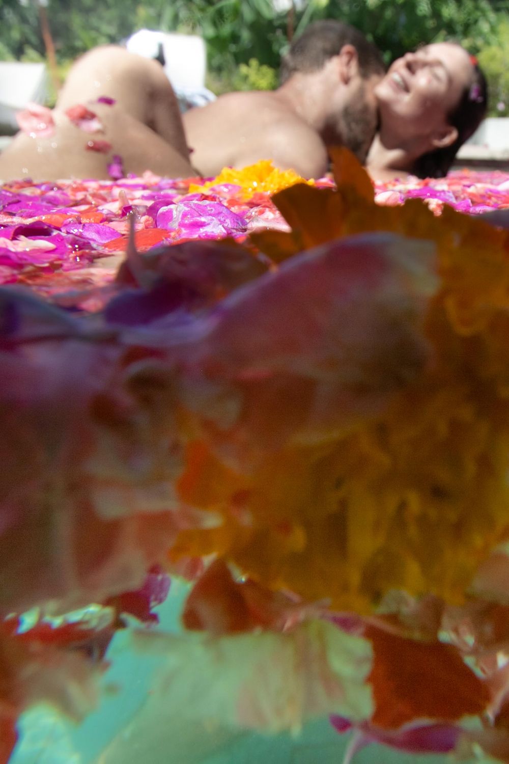 A man kissing a woman's neck in a pool of floating flowers
