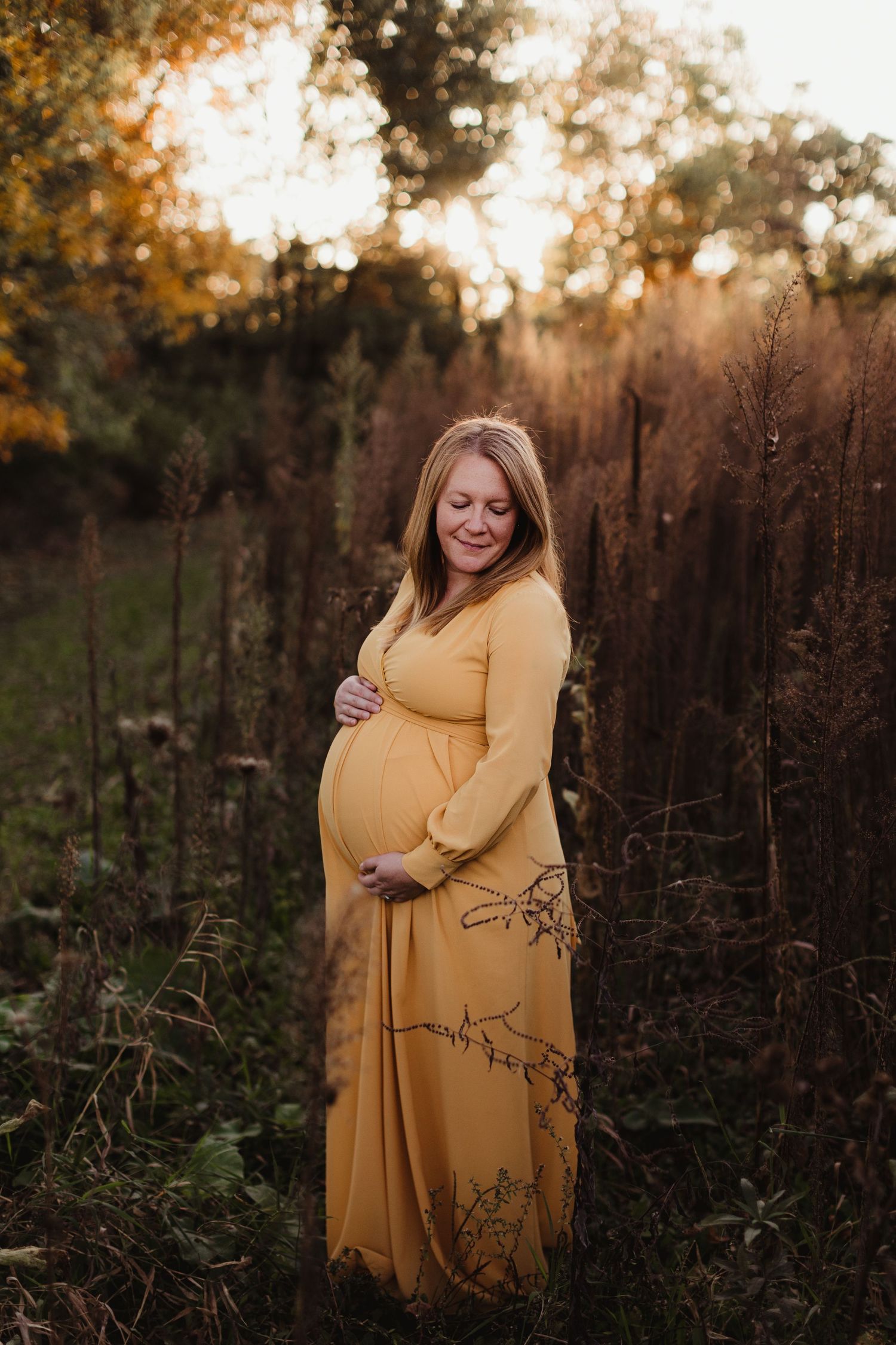 A woman cradles her pregnant belly during a golden sunset. Photo by maternity photographer, Elizabeth Pachniak.