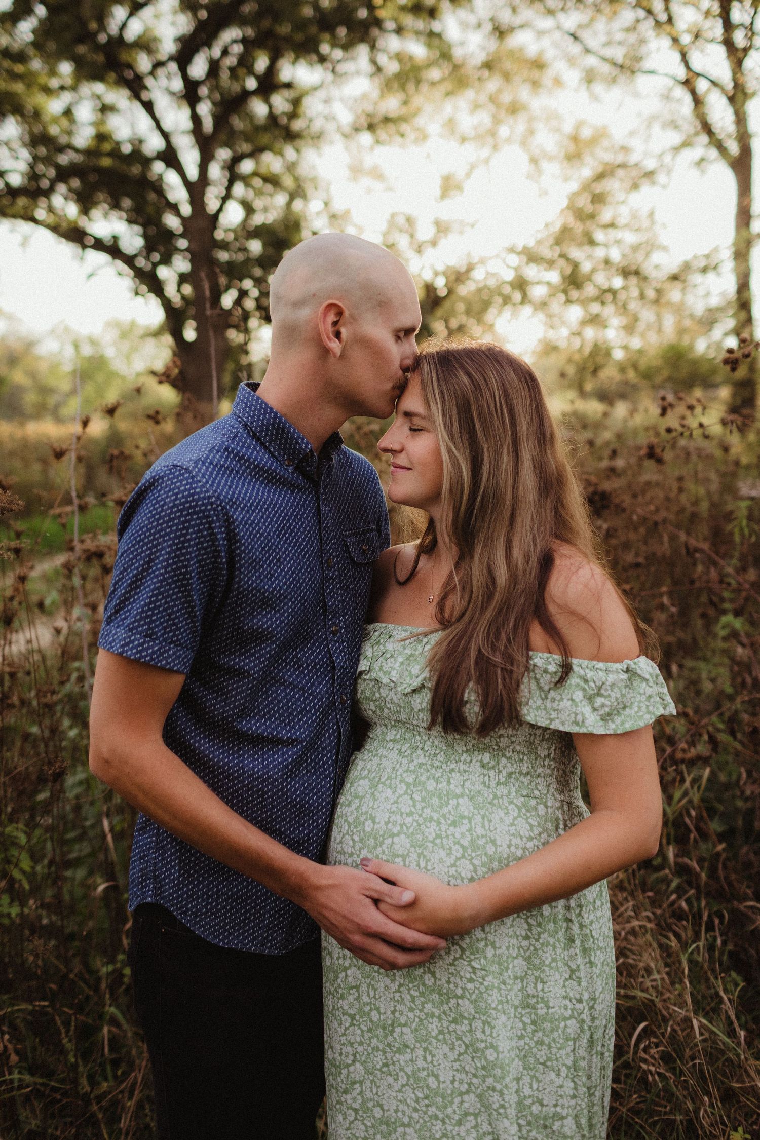 An expecting mom and dad cradle moms pregnant belly at sunset. Photo by maternity photographer, Elizabeth Pachniak.