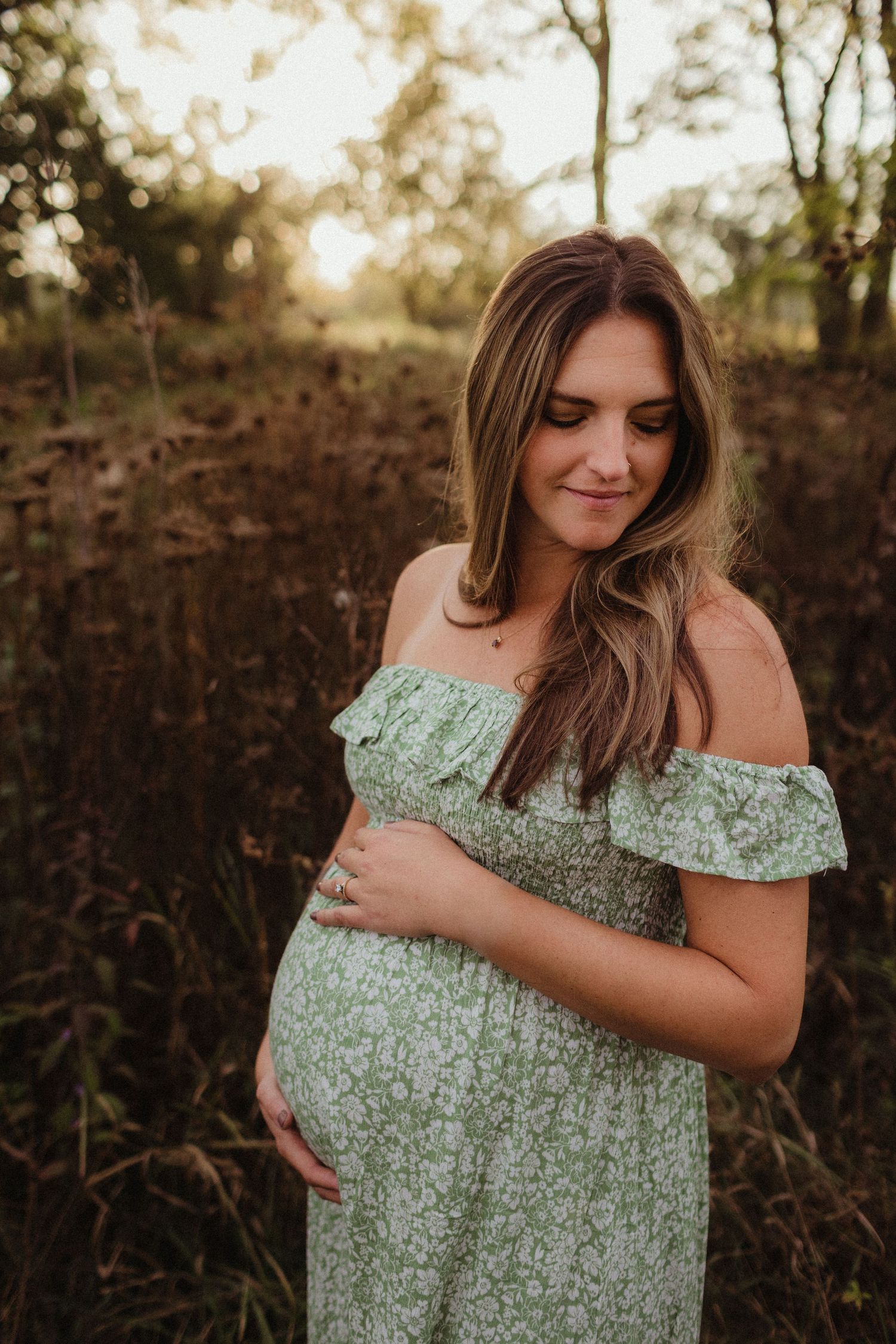 A woman cradles her pregnant belly at sunset. Photo by maternity photographer, Elizabeth Pachniak.