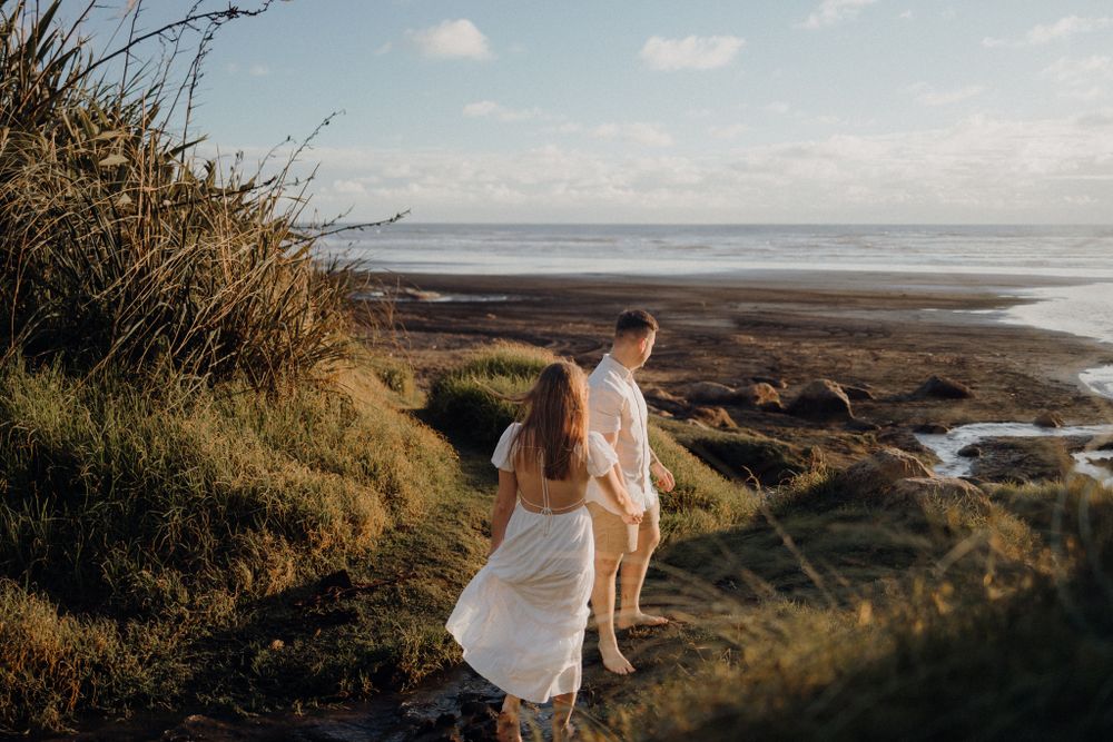 A couple walks down a coastal path overlooking the ocean during golden hour.