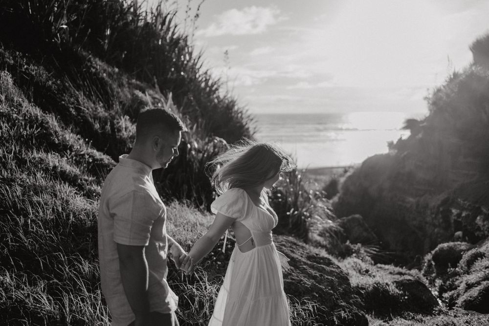 A black and white photo of a couple sharing a playful moment on a coastal hillside.
