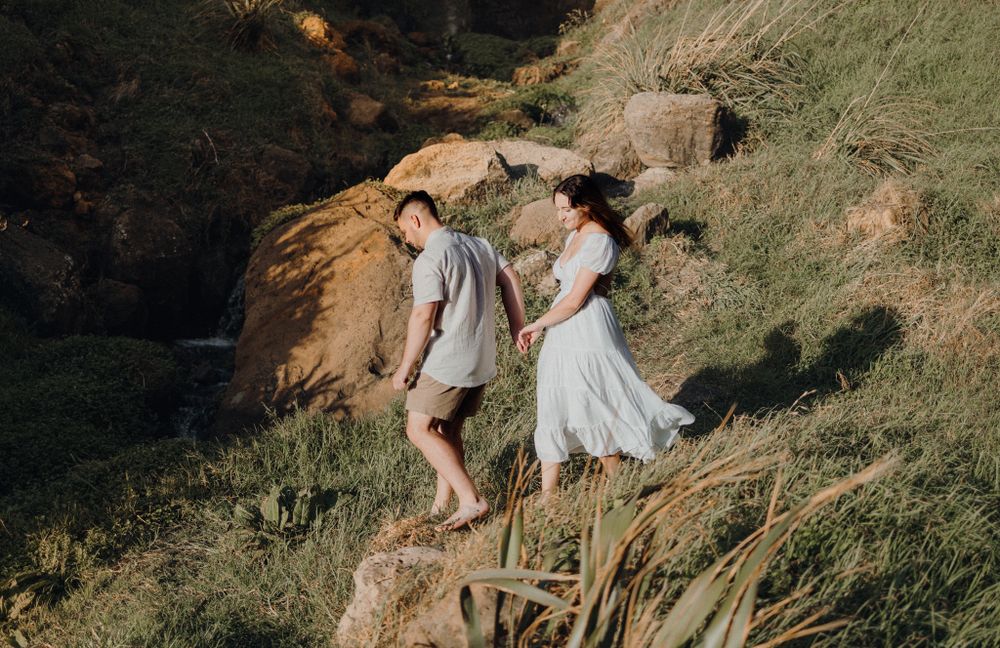 A couple holding hands while walking down a grassy coastal slope.