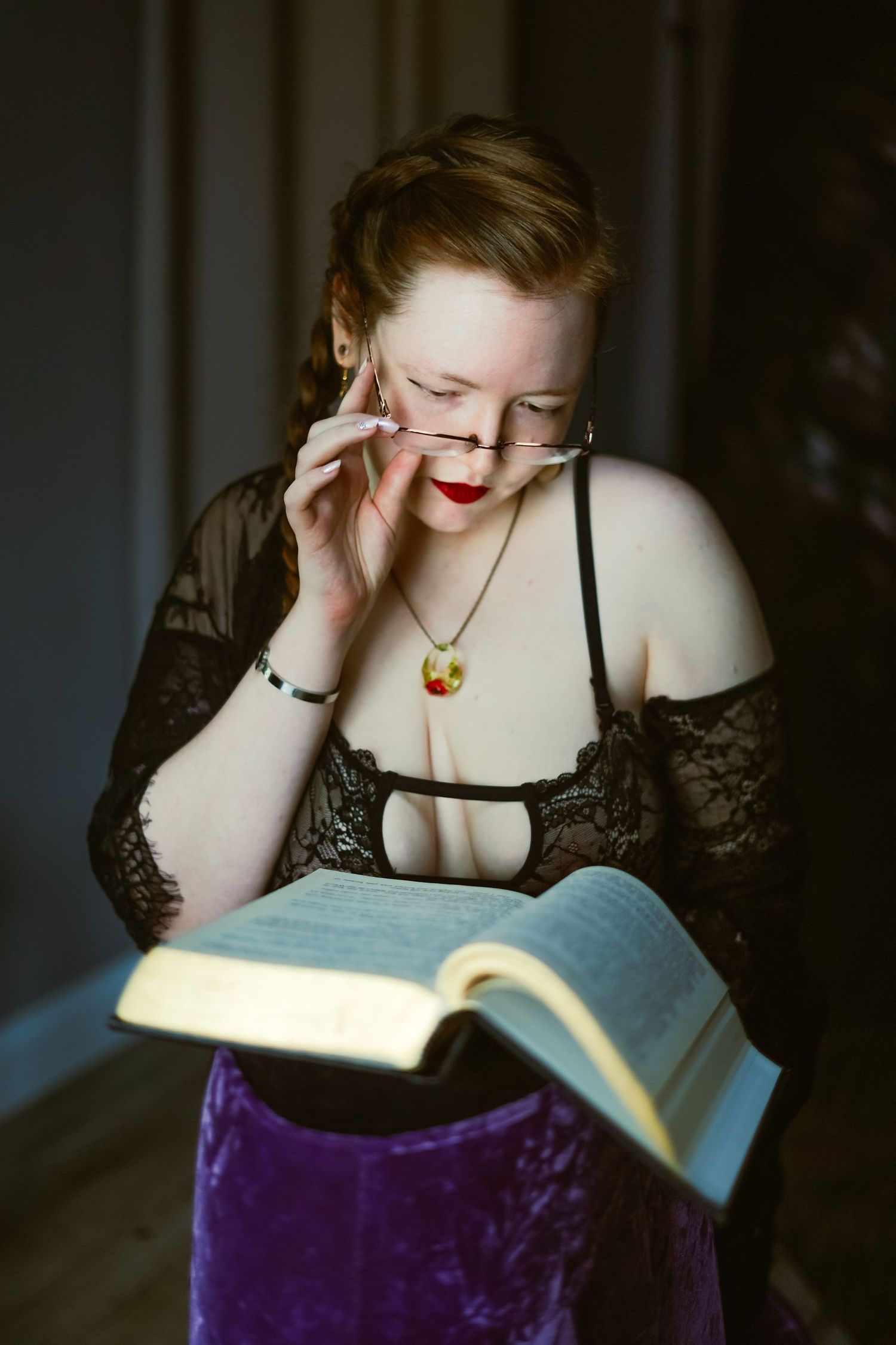 A studious model in black lace adjusts the glasses low on her nose as she reads a book.