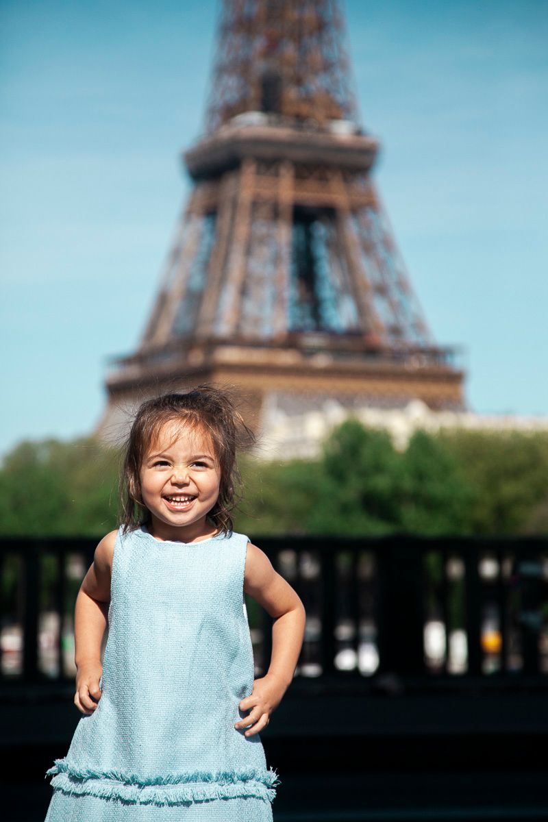 Young child in light blue dress poses in front of the Eiffel Tower.