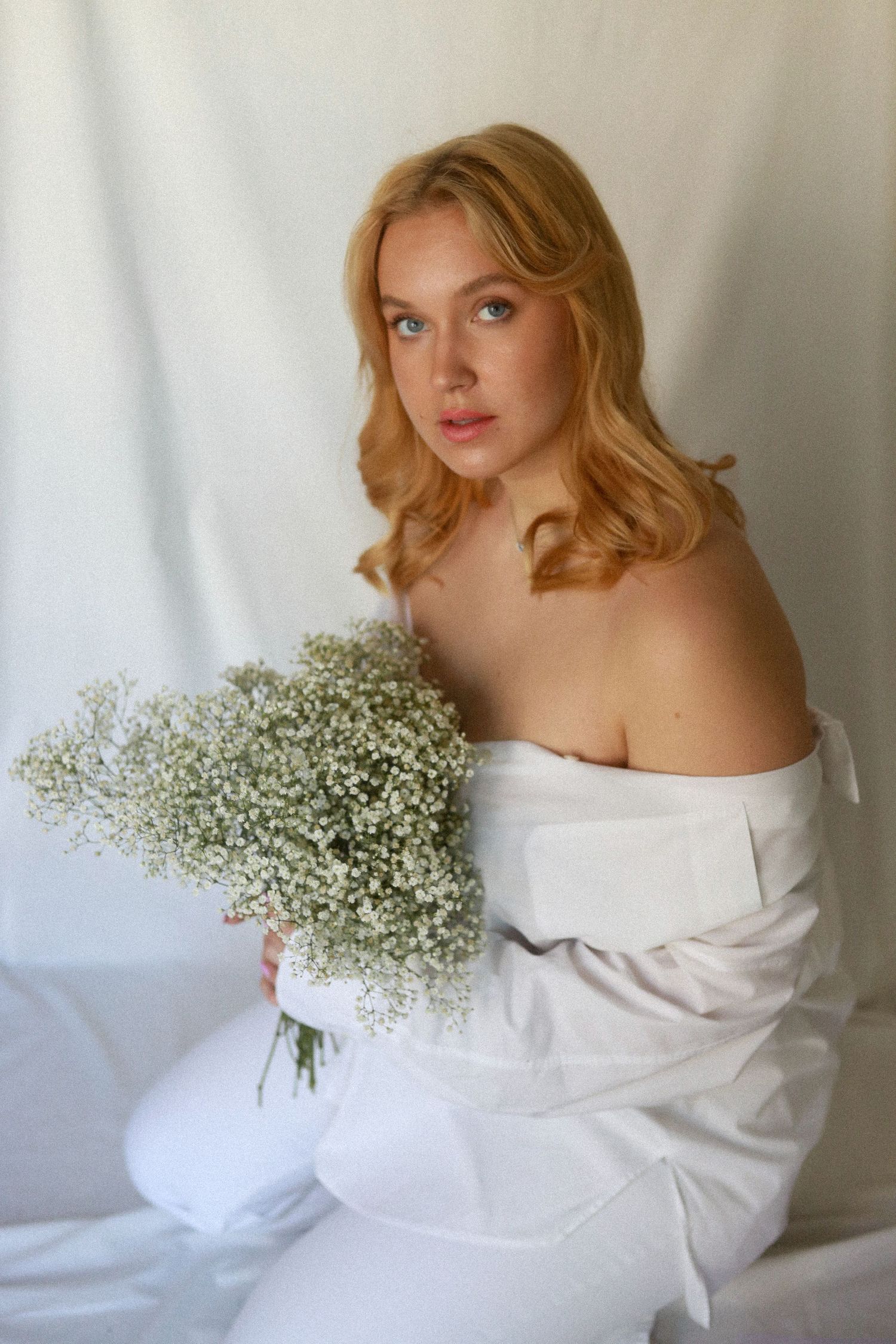 A soft portrait of a woman in white holding baby's breath flowers against a light background.