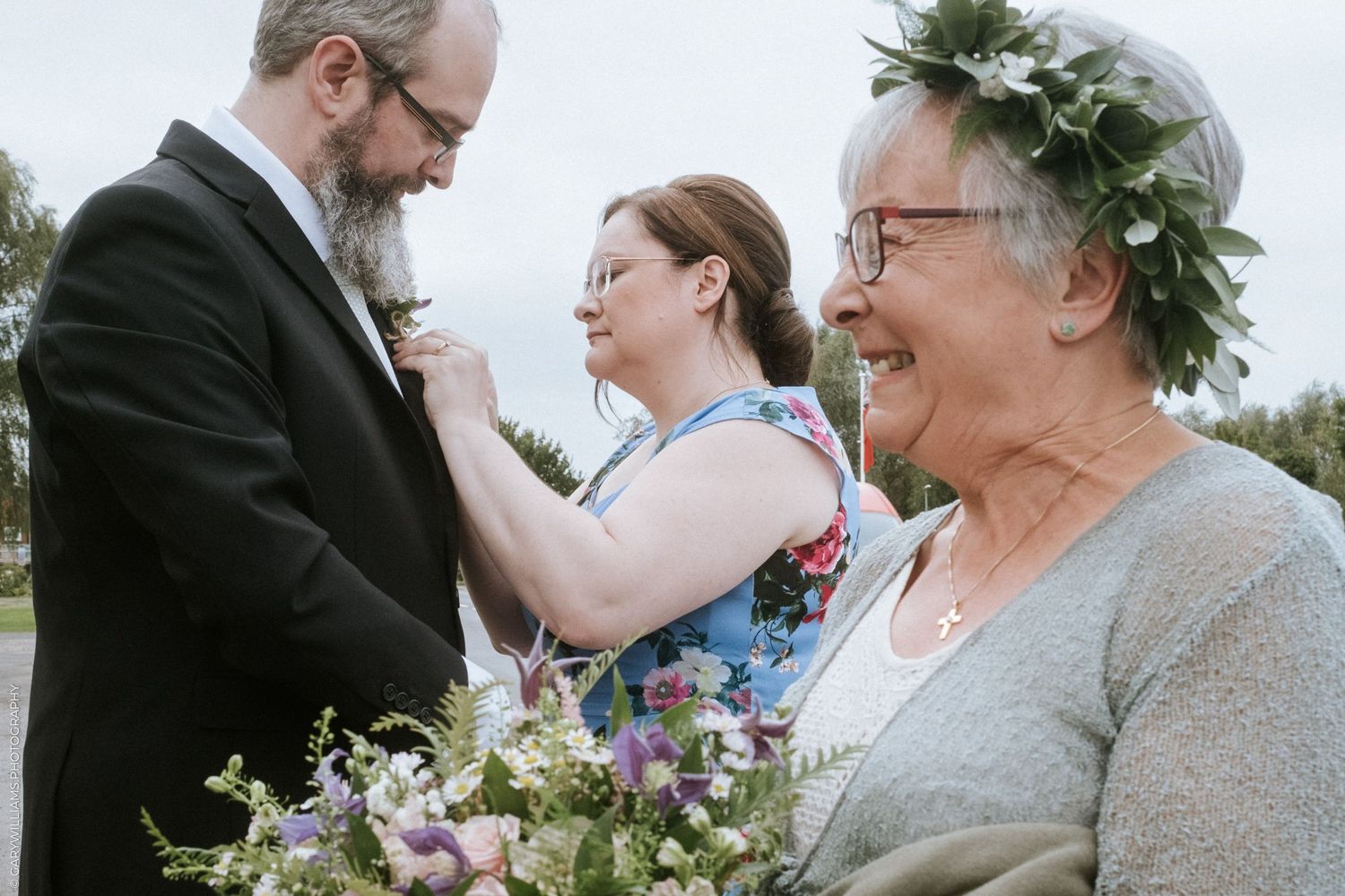 Bride smiling and a the best man having his boutonniere fixed at a wedding at St. James Baptist Church in Lincolnshire