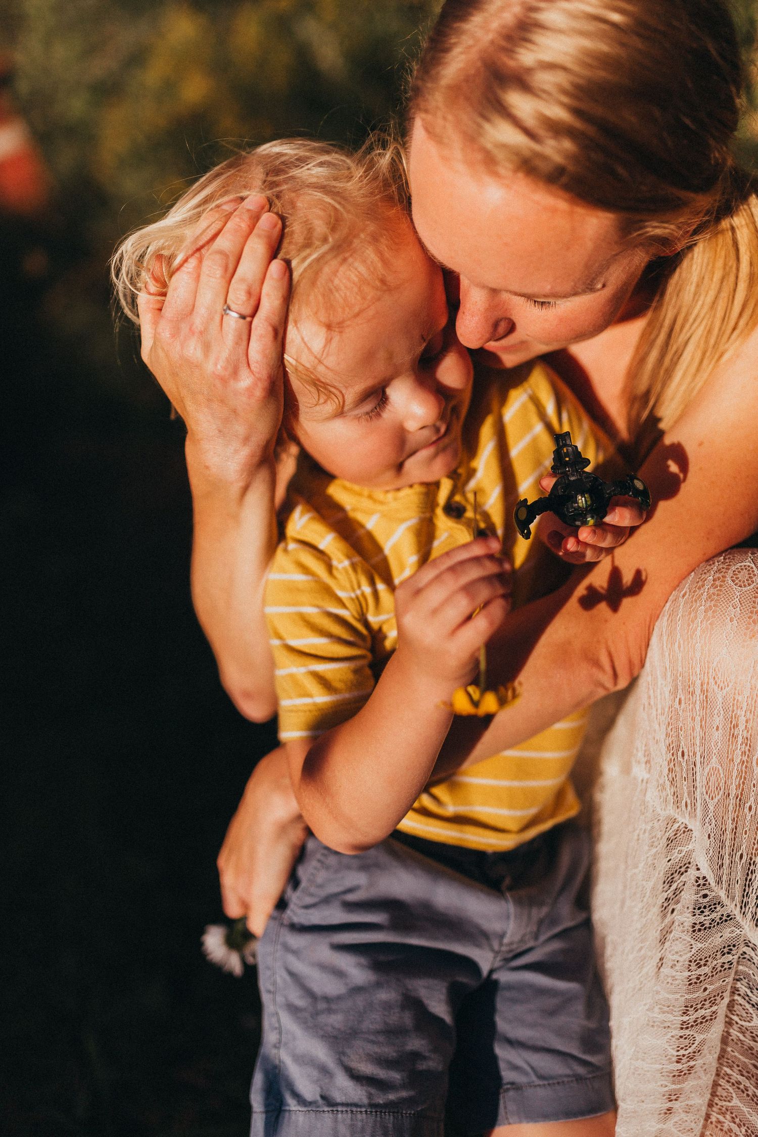 Sweet sunset moment of affection with child in yellow striped shirt being embraced.