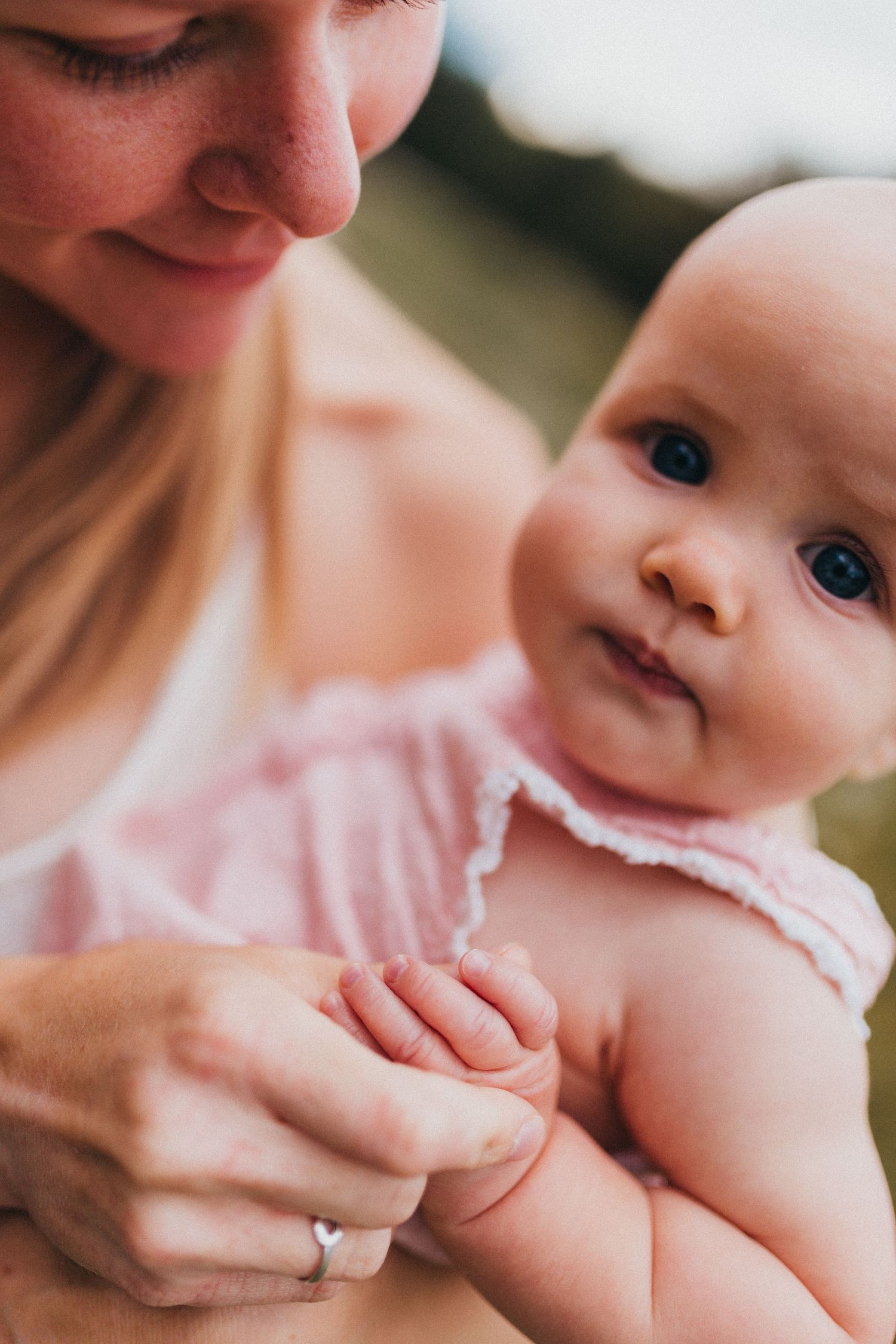 Baby wearing pink smiles while being held by caregiver in intimate close-up portrait.