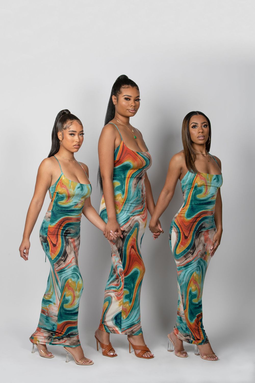 Three models in matching swirled print dresses pose together against white background.