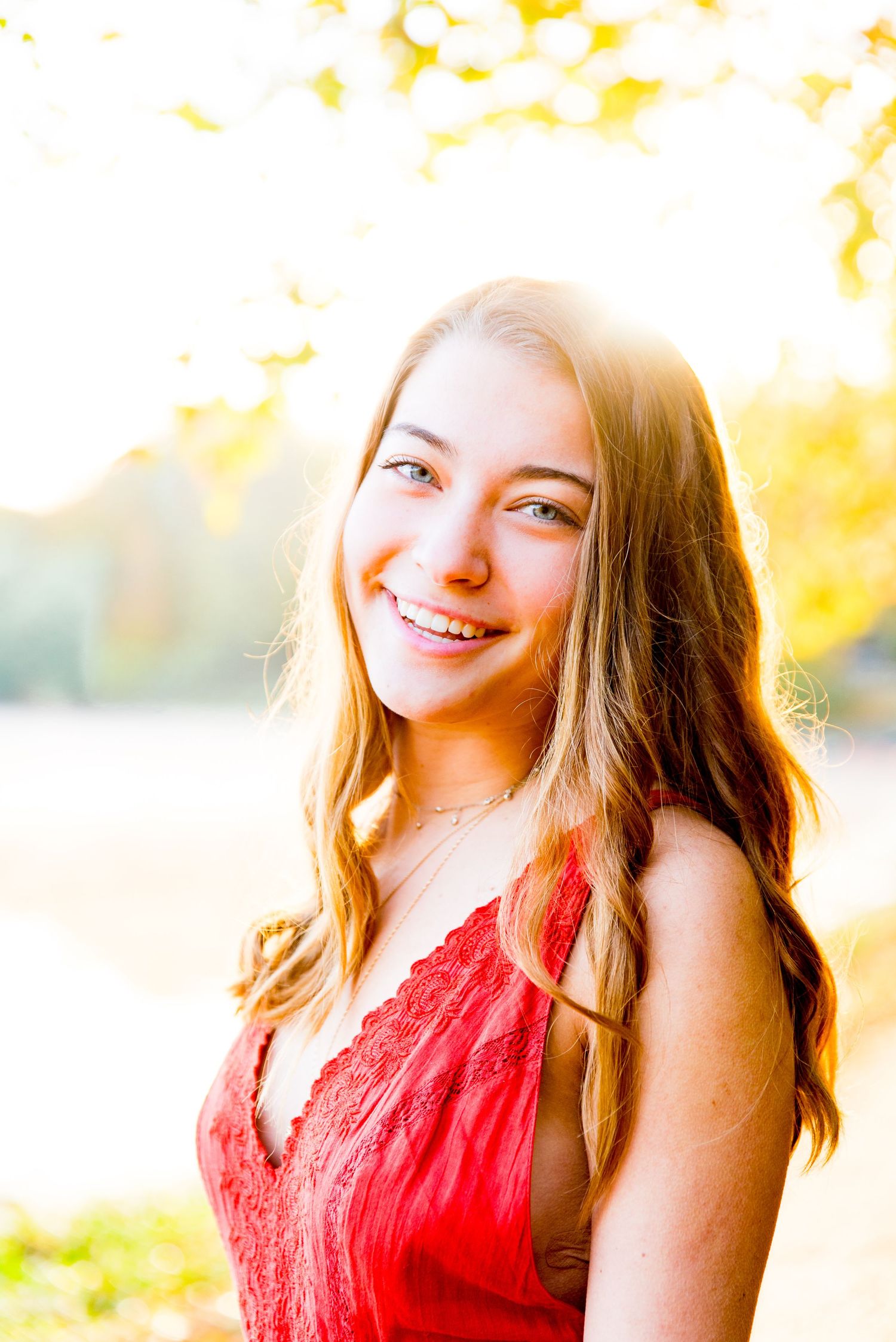 young woman with blue eyes smiles under a yellow fall tree at sunrise at Montrose Harbor in Chicago for senior pictures