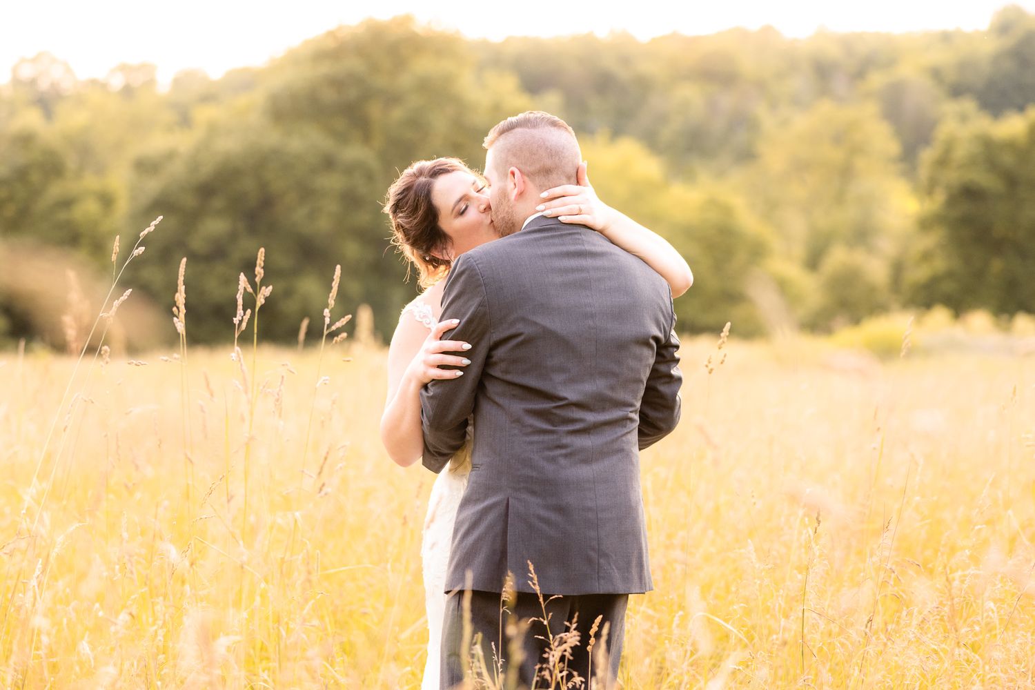 Golden Hour Wedding Photo of Couple Kissing in Tall Grass During Wedding at Magnolia Spring Farm in Magnolia, Ohio