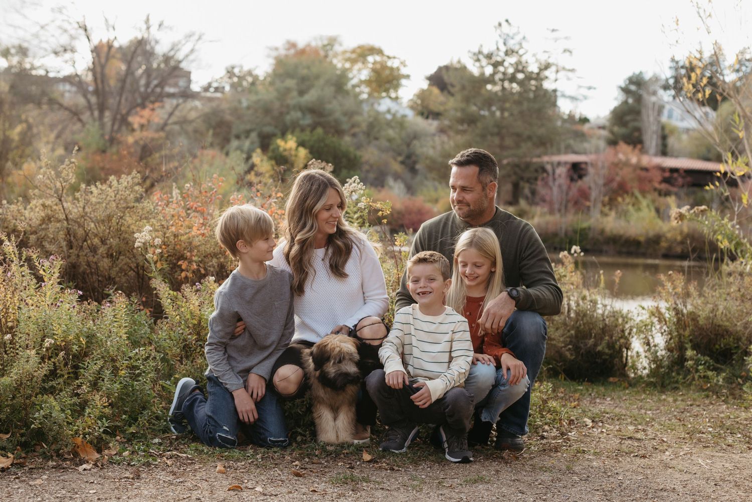 A family with their puppy smiles at each other while taking family photos at a park near downtown Boise in the fall.