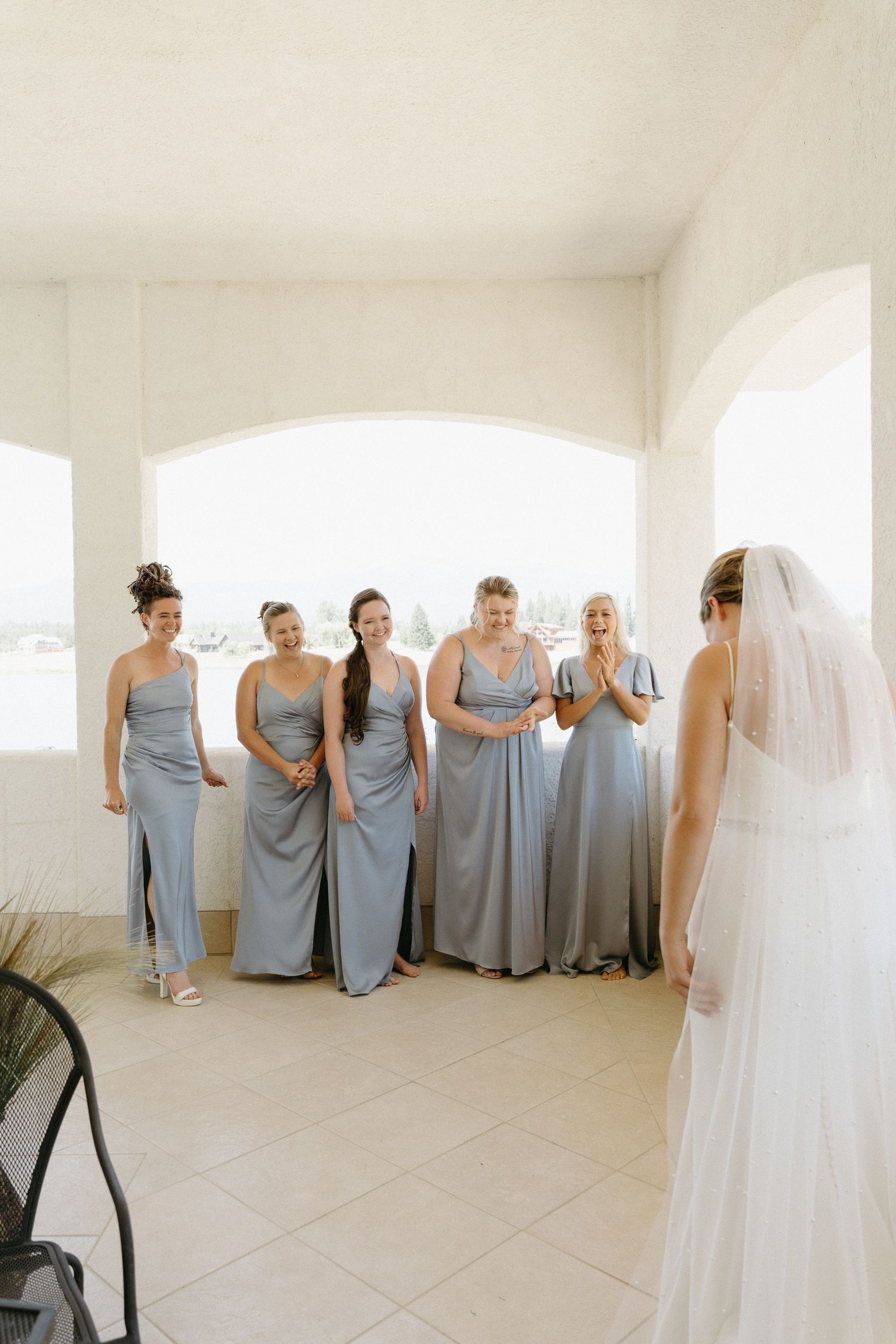 Bridesmaids in matching blue gowns gather in an elegant white arched room.