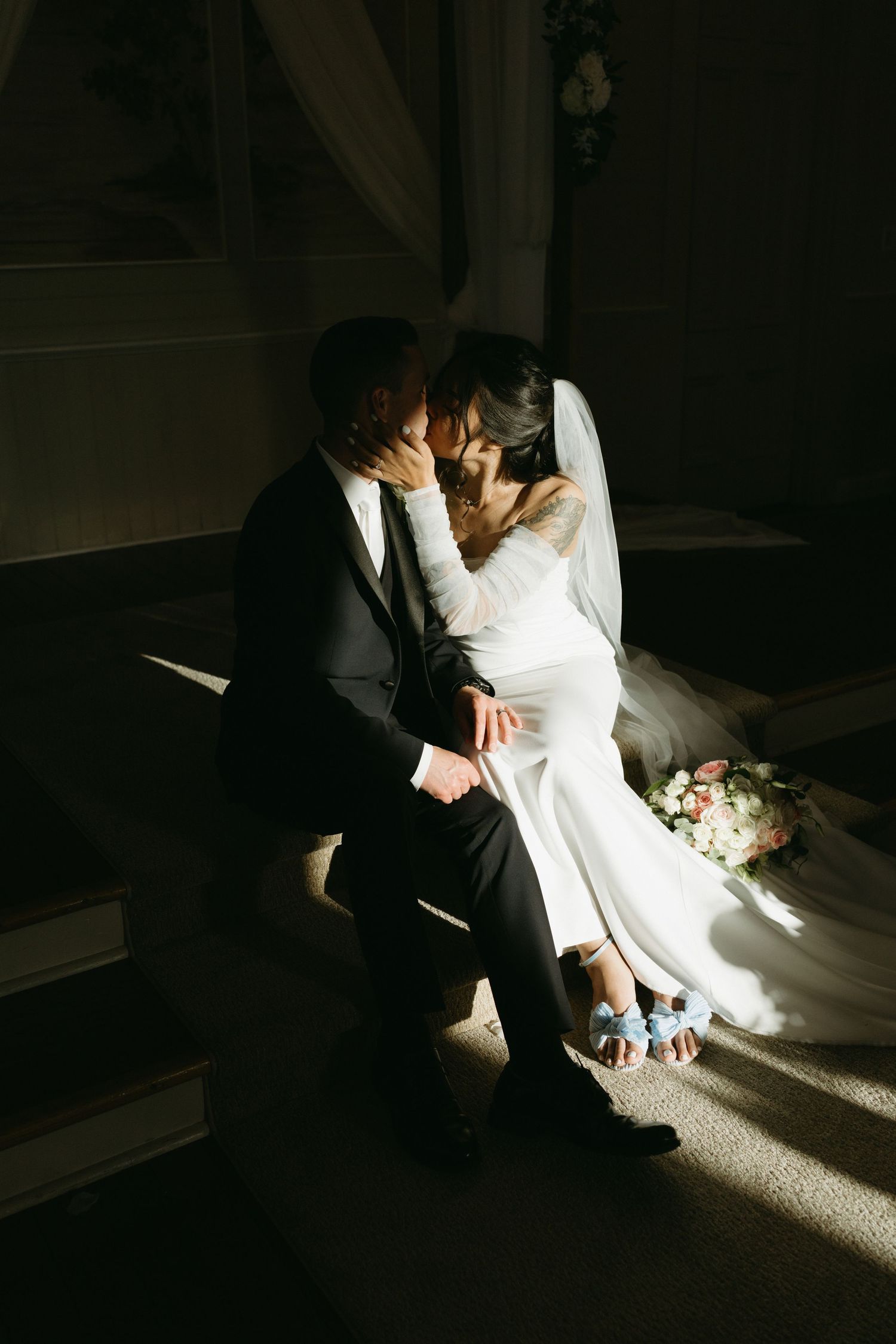 A dramatic moody wedding portrait with natural light streaming through a window.