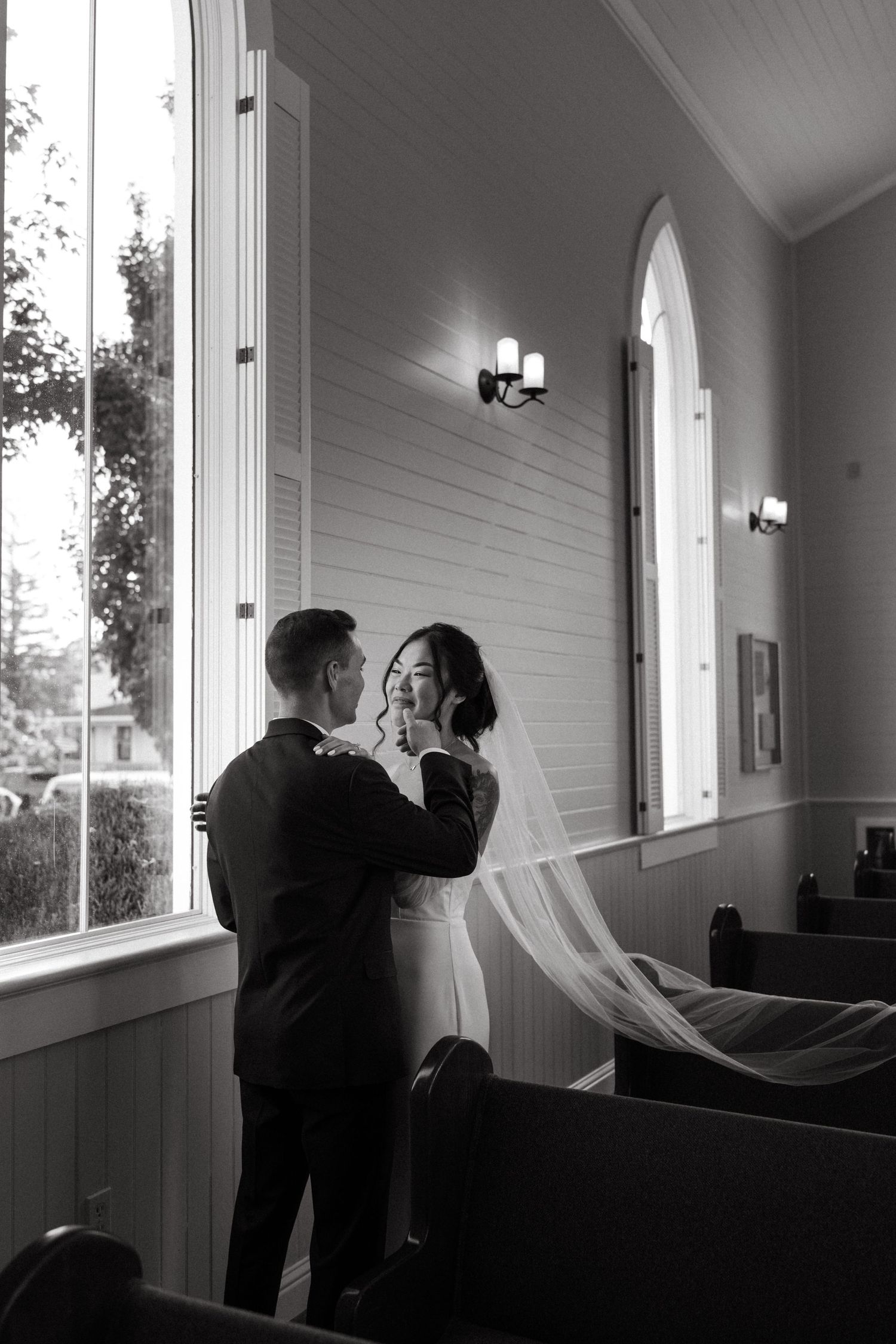 An intimate black and white wedding moment captured in a chapel setting with natural window light.