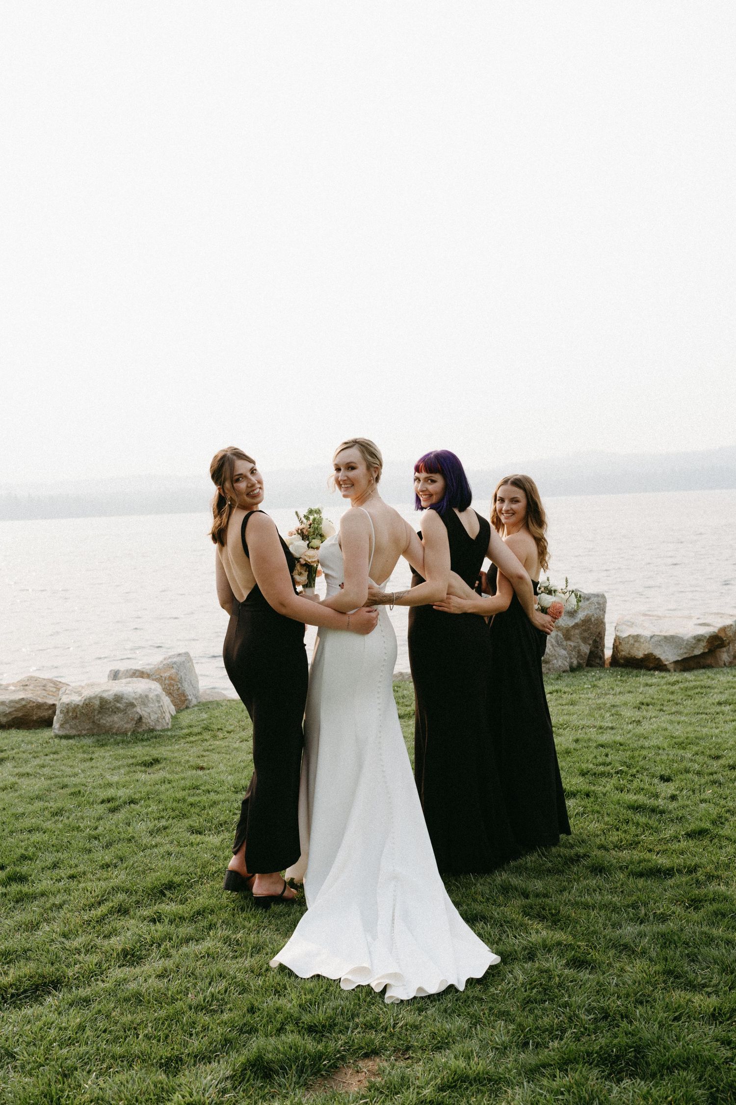 Wedding party in black and white dresses posing on cliffside overlooking water.