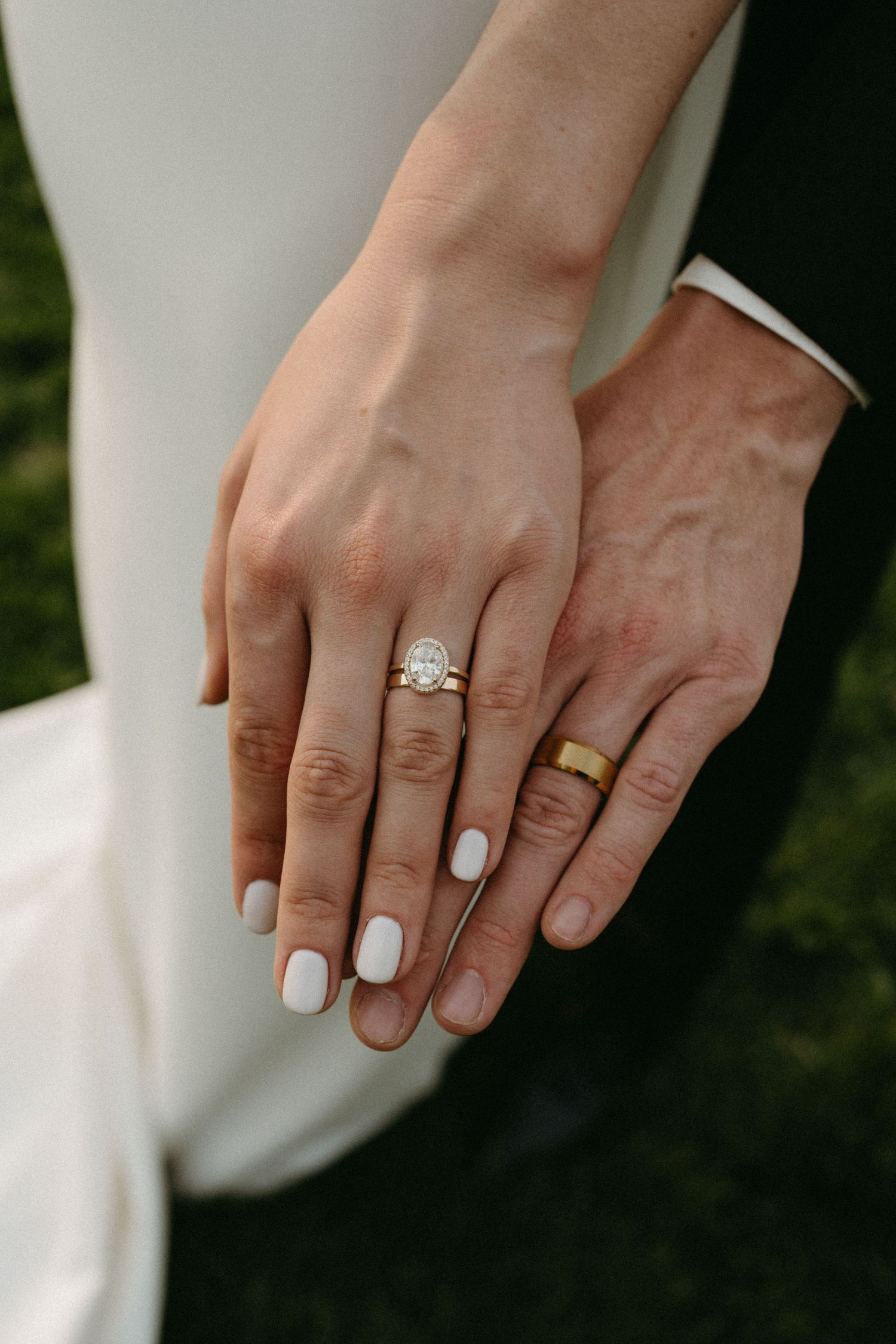 Close-up of newlyweds' hands showing wedding rings and white nail polish.