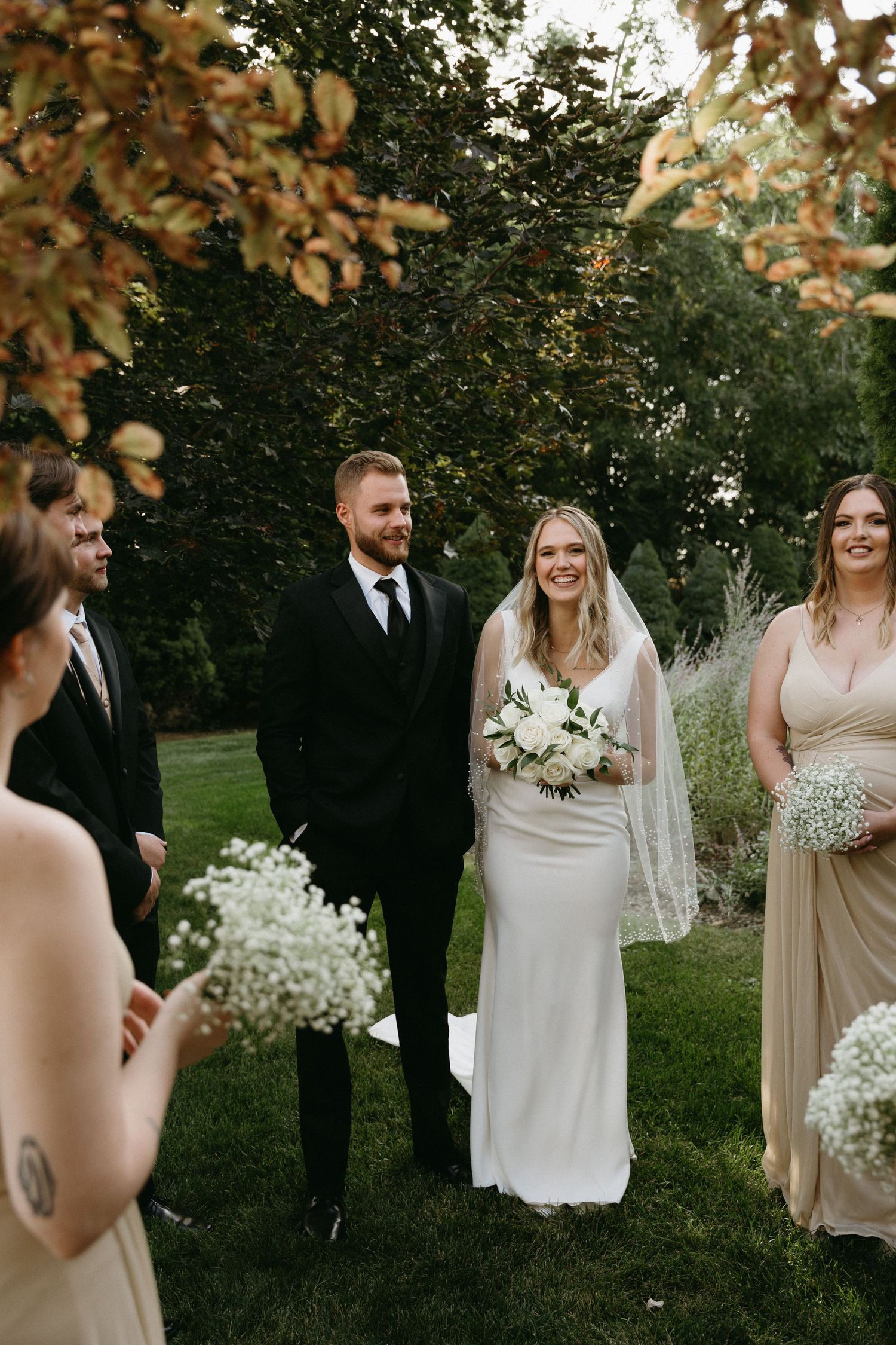 A wedding party gathering outdoors with autumn foliage in the background.