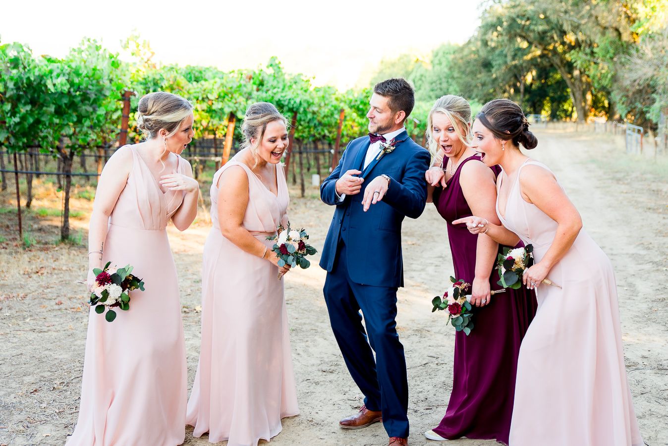 bridesmaids in blush dresses gawk at groom's wedding ring