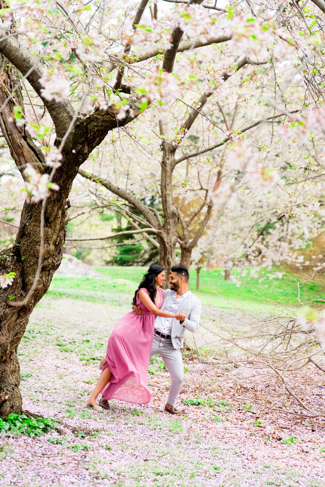 Woman in pink dress and man in gray suit dancing on steps to Bethesda Terrace Central Park for spring engagement photos