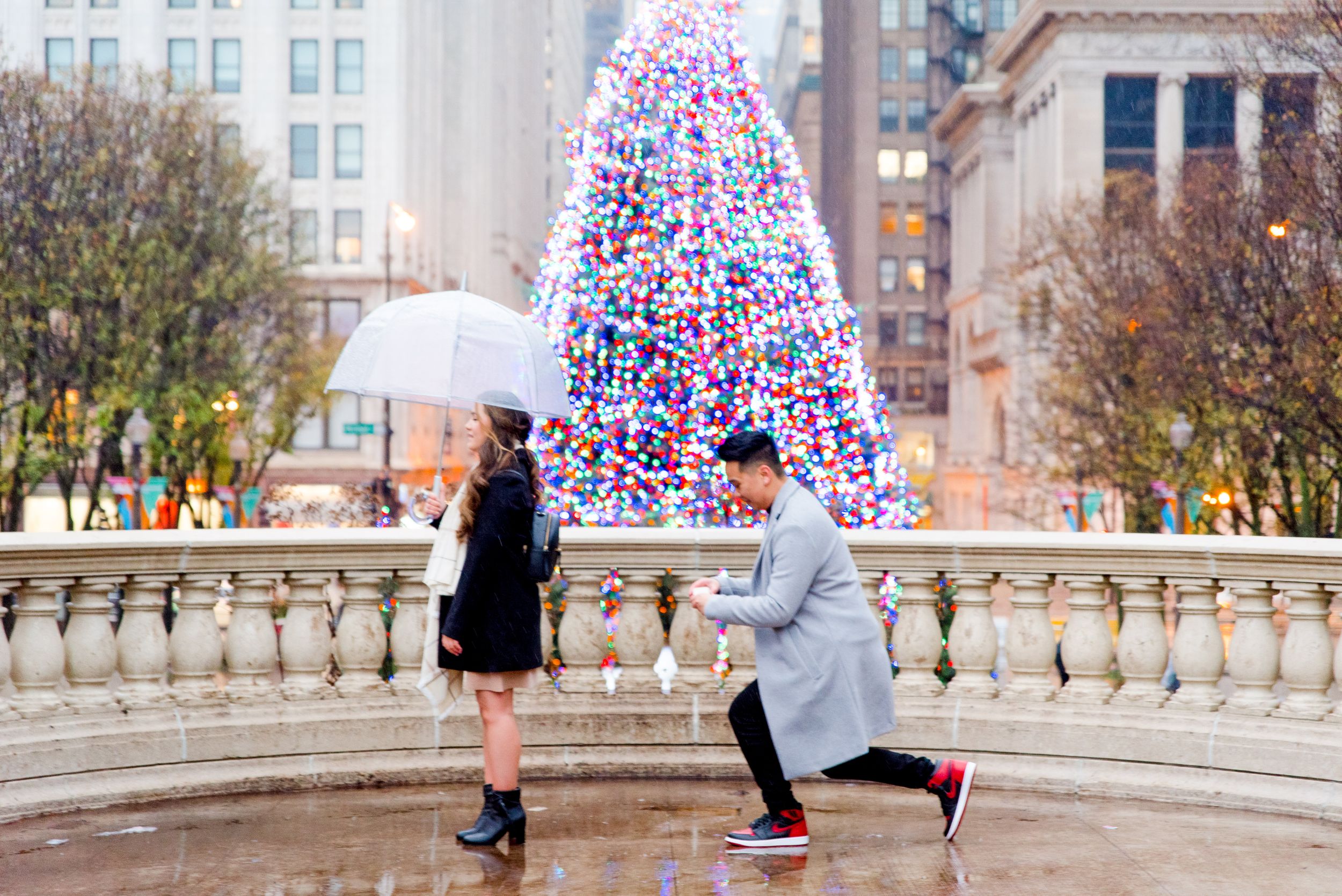 Man in gray coat kneeling down in front of Christmas Tree at Millennium Park in Chicago about to propose