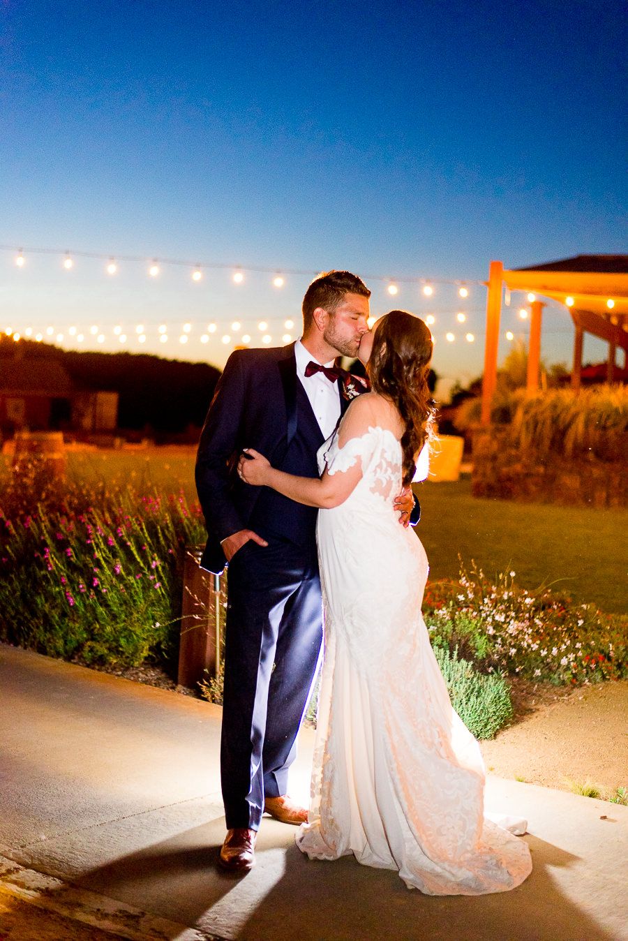 bride and groom kiss in front of string lights and dark blue sky at Pennyroyal Farm wedding