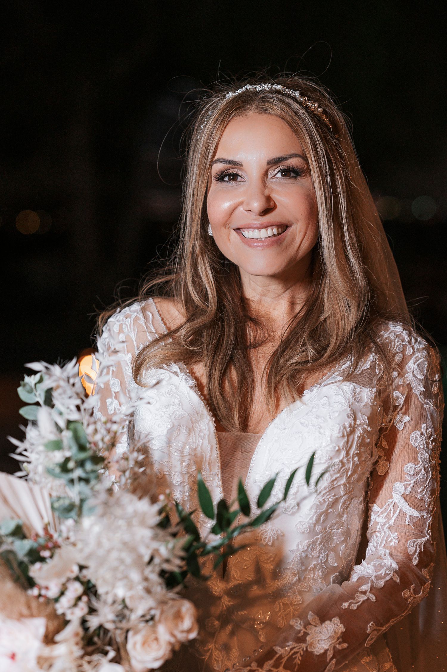 Person in white lace wedding dress holding bouquet of flowers.